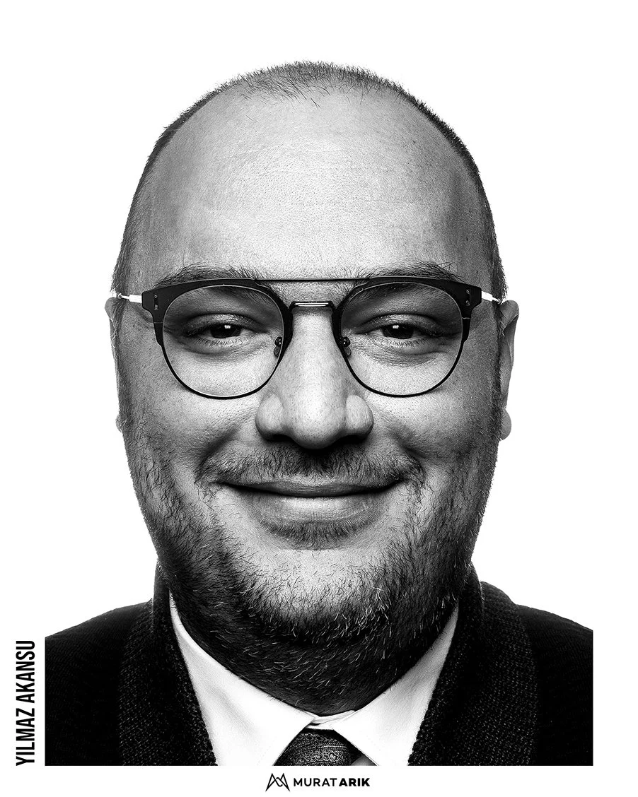 Black and white portrait of Yilmaz Akansu wearing glasses, smiling, in a collared shirt and jacket.
