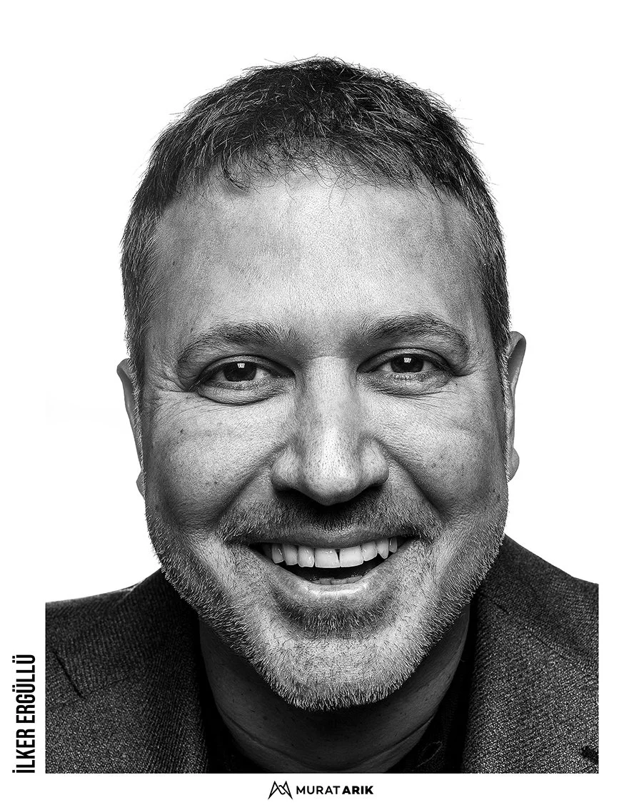 Black and white portrait of a smiling man with short hair and a beard, wearing a dark suit jacket.