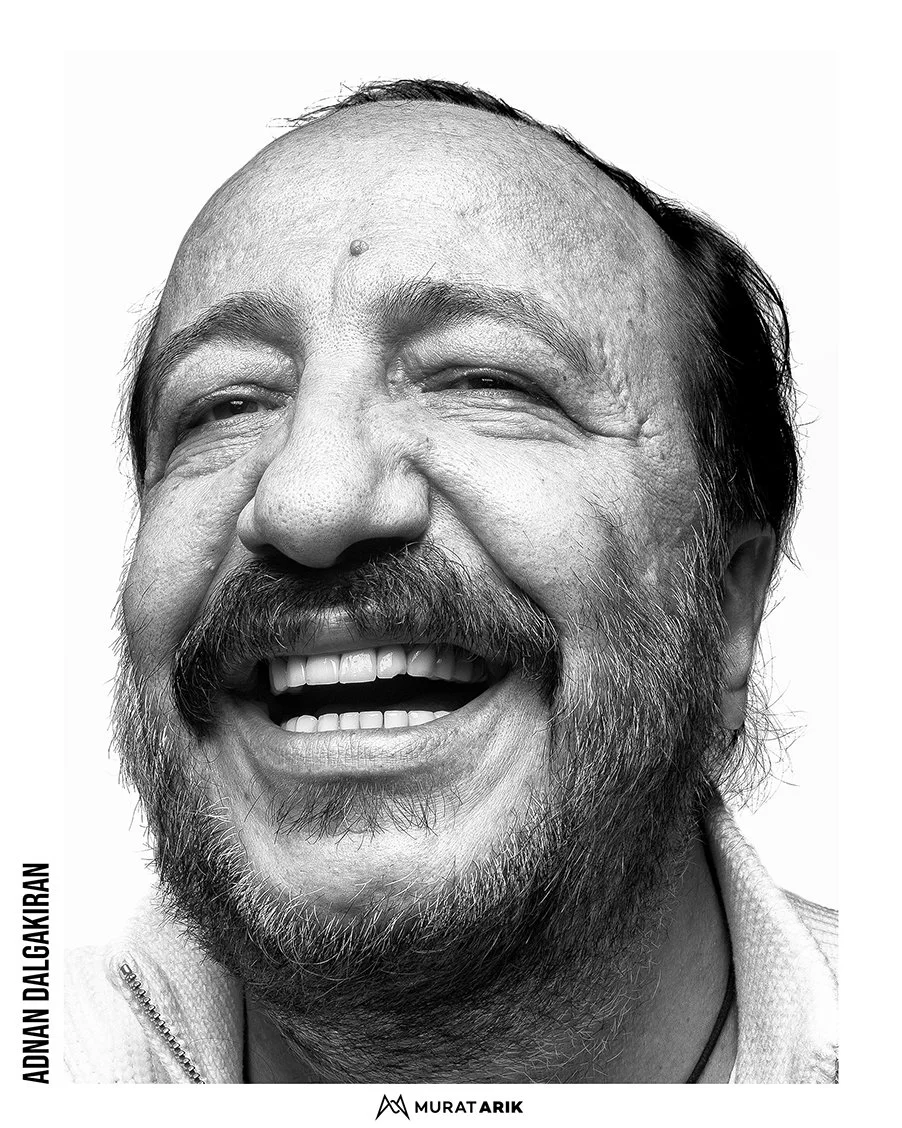 A black and white close-up of a man with a beard and mustache, smiling broadly with his eyes slightly squinted.