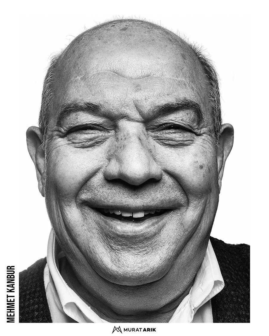 A smiling black man with short hair, wearing a white shirt and dark sweater, photographed in black and white.