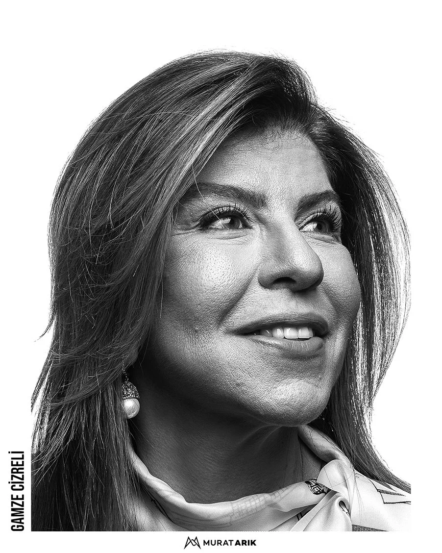 Black and white portrait of a woman with long hair, smiling and looking slightly upward, wearing earrings and a scarf.