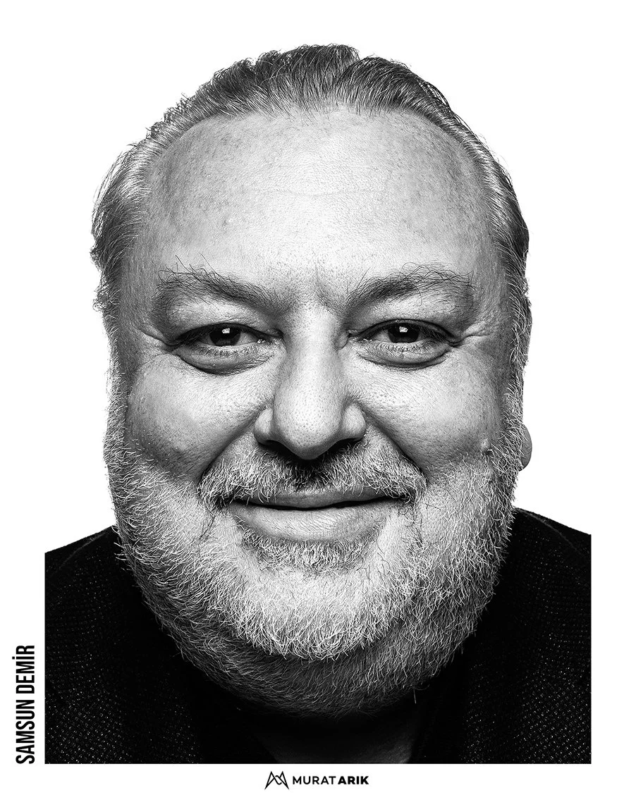 Black and white close-up portrait of a smiling middle-aged man with a beard and short hair, wearing a dark top.