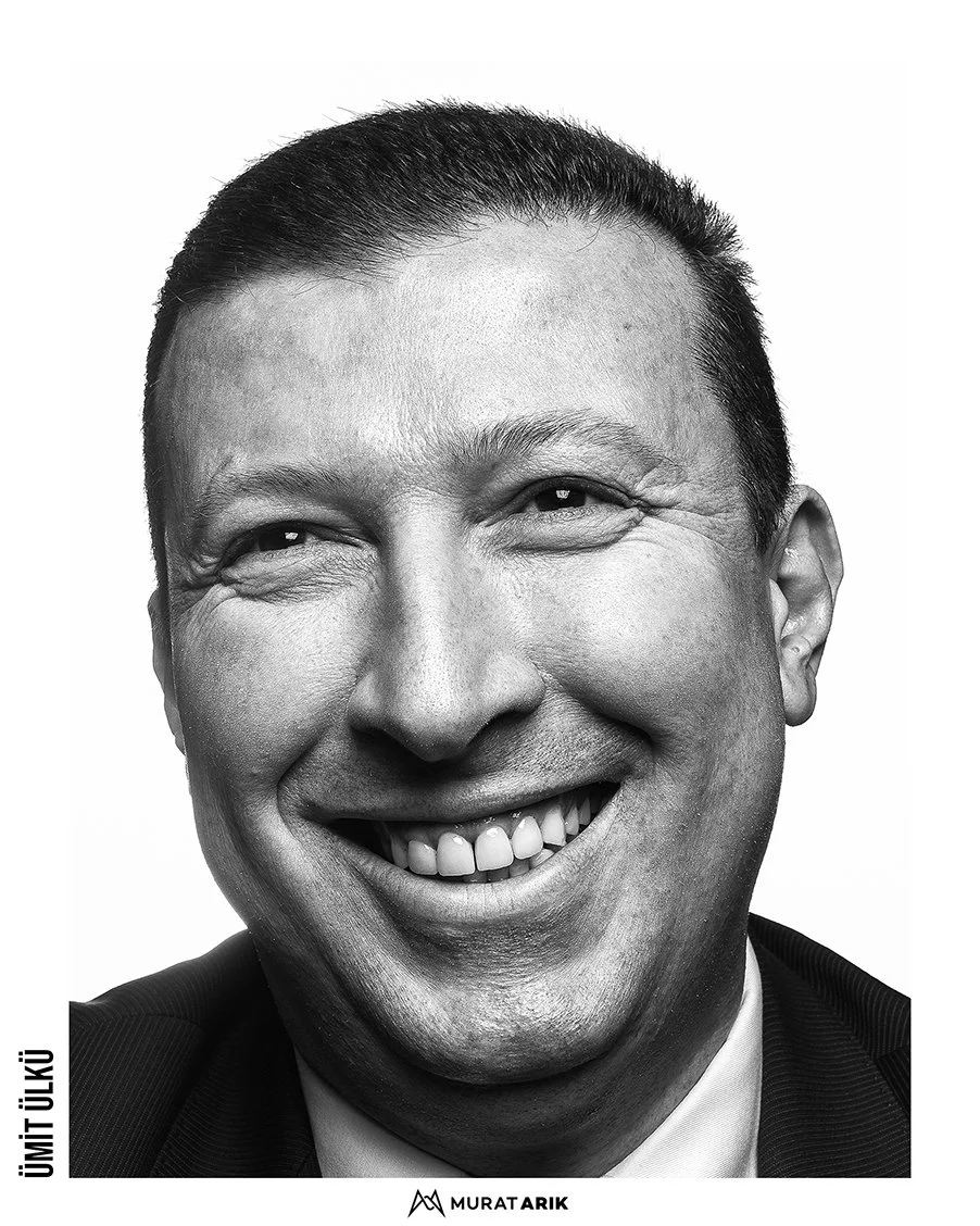 A close-up black-and-white photo of a smiling middle-aged man with short, dark hair, wearing a suit and white shirt.