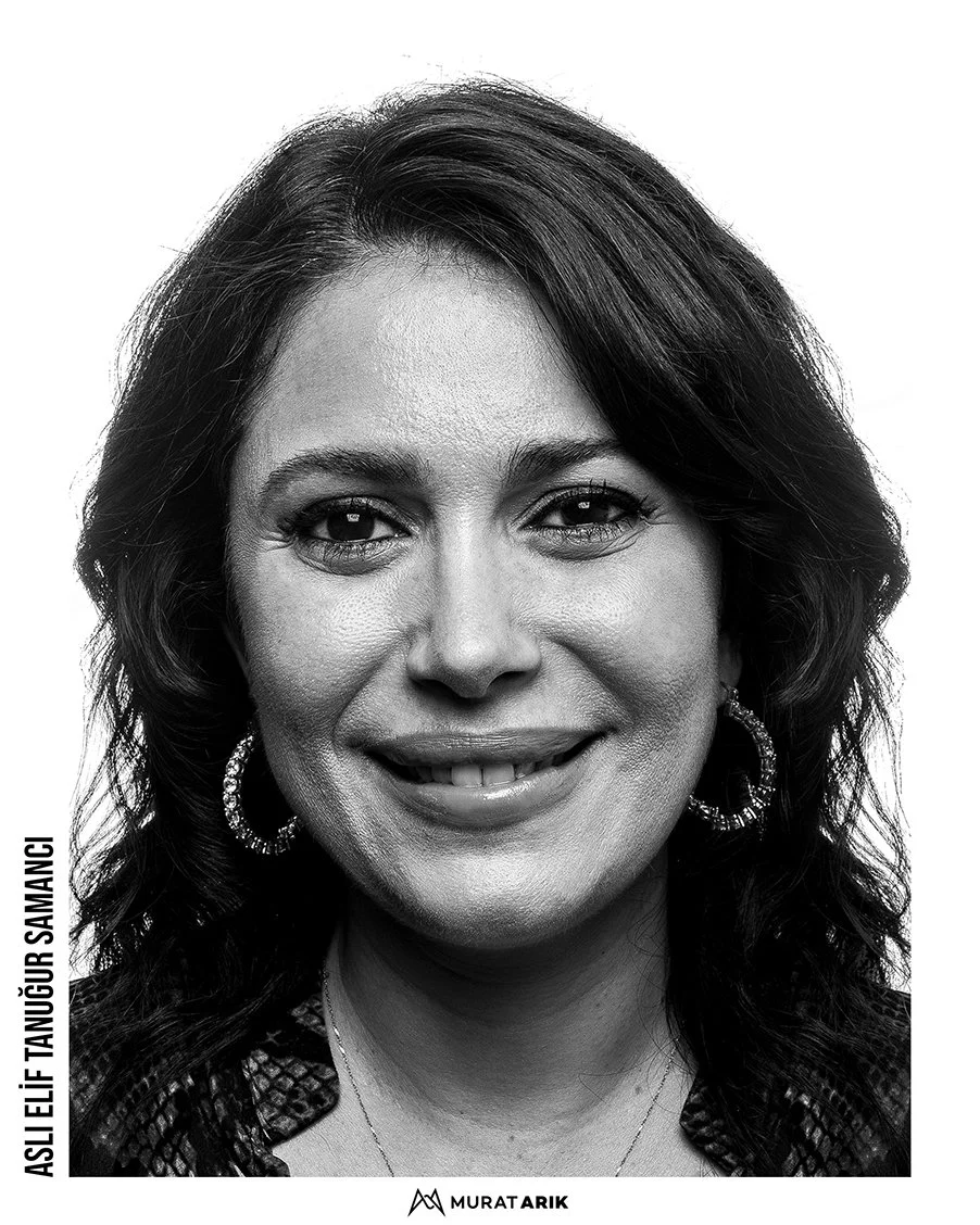 Black and white portrait of a woman smiling, with shoulder-length wavy hair, hoop earrings, and a textured top.