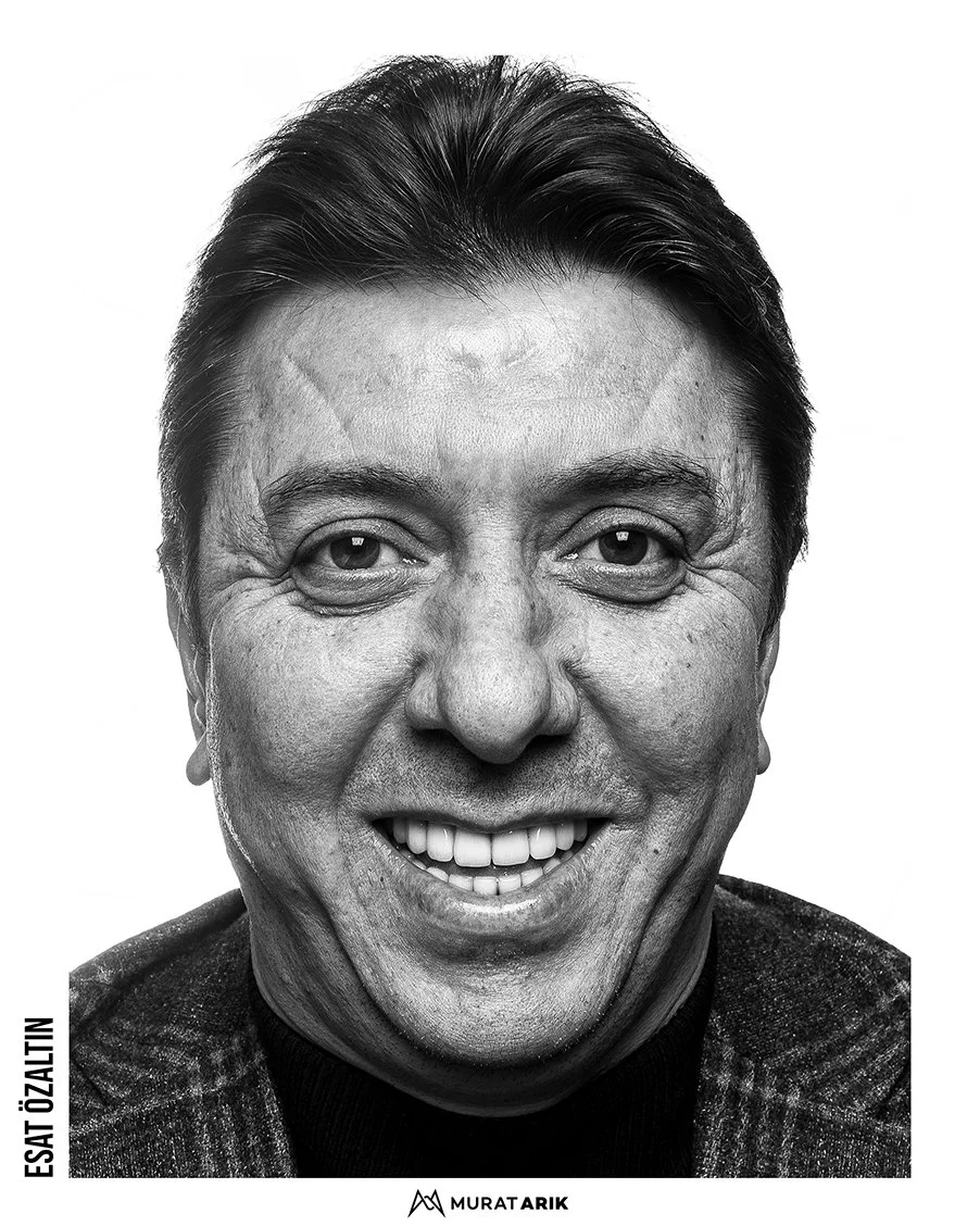 Close-up black and white portrait of a smiling man with short dark hair and light skin, wearing a checkered blazer.