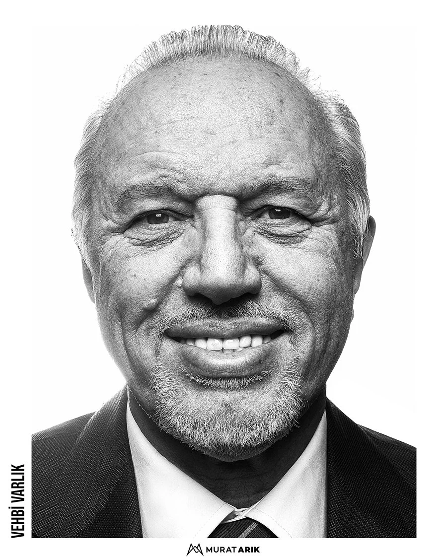 Black and white close-up portrait of an elderly man with a receding hairline, gray facial hair, and a broad smile showing his teeth, wearing a suit and tie.