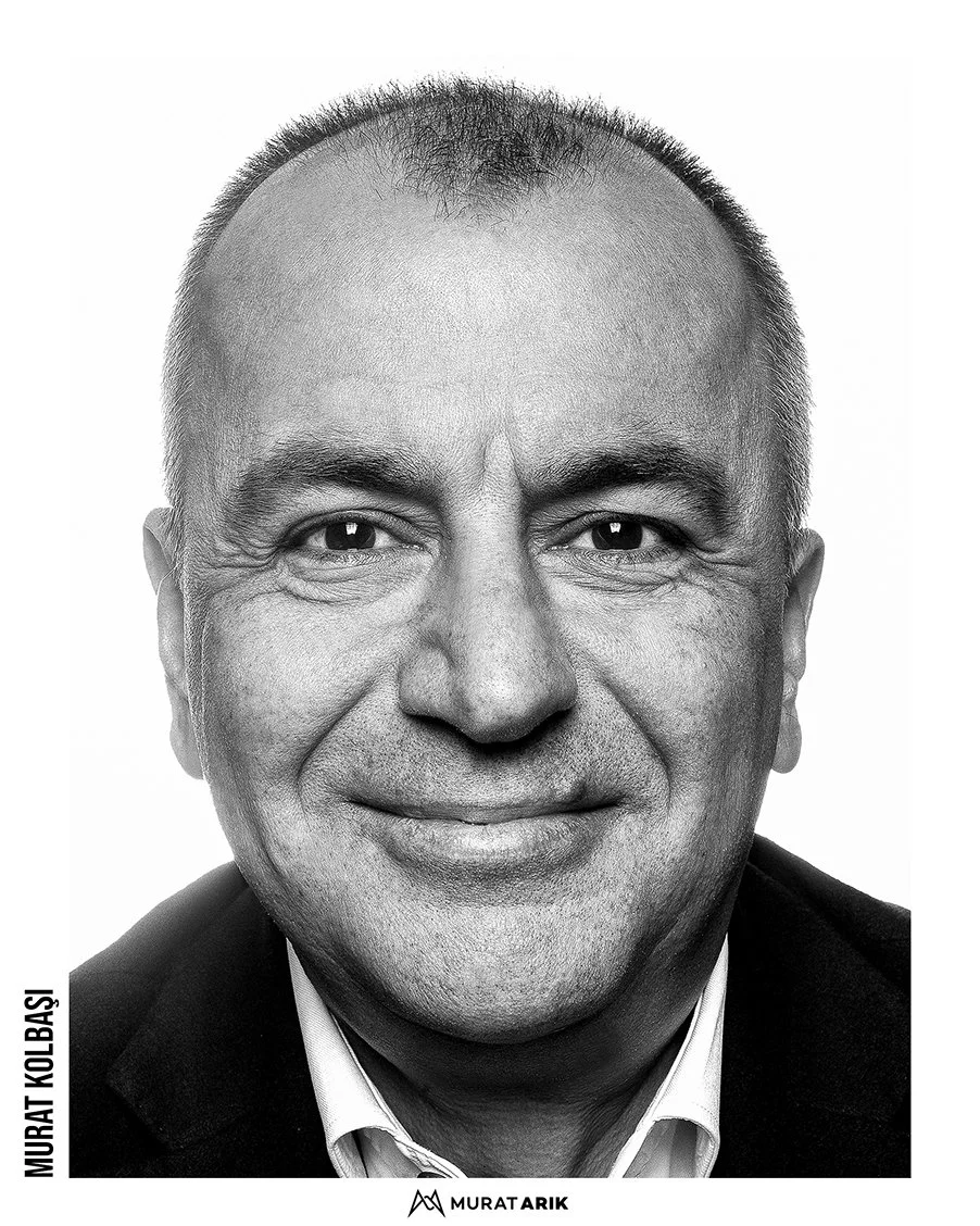 Black and white portrait of a middle-aged man smiling, wearing a dark blazer and a collared shirt.