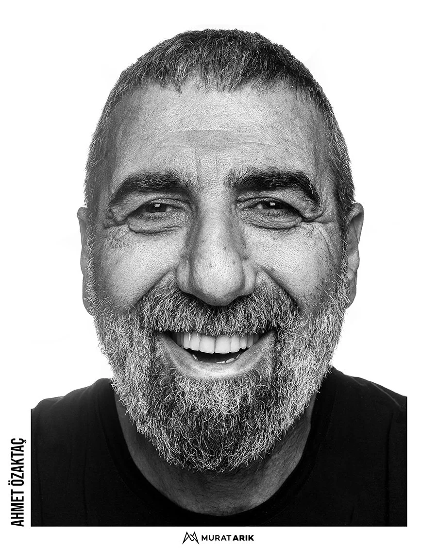 Close-up portrait of smiling middle-aged man with a beard, short hair, and wearing a black shirt, against a plain white background.