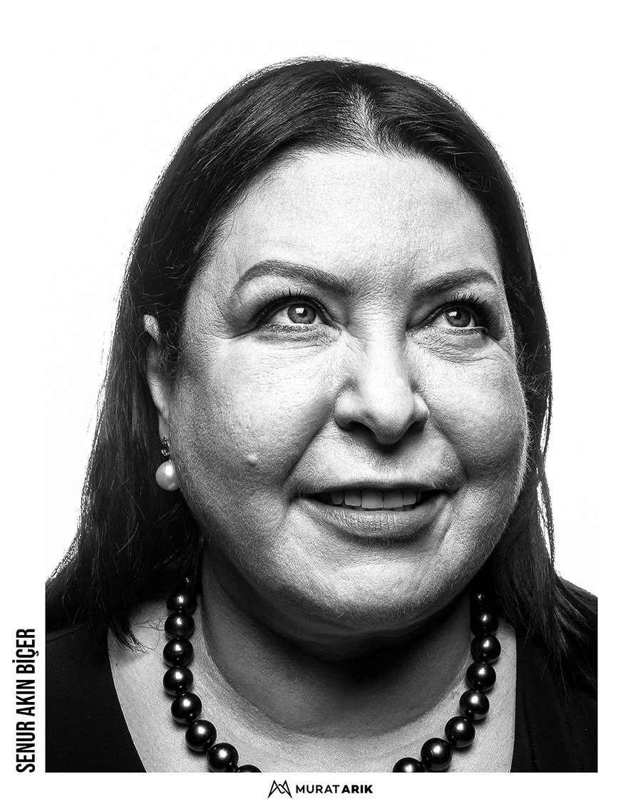 Black and white portrait of a woman with dark hair, pearl earrings, and a pearl necklace, smiling and looking slightly upward.