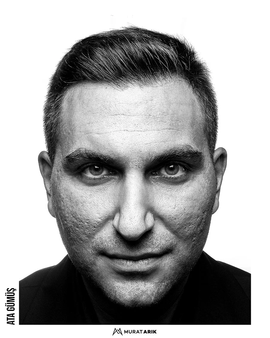 Black and white close-up portrait of a man with short, neatly styled hair, intense eyes, and a subtle smile, wearing a dark shirt.