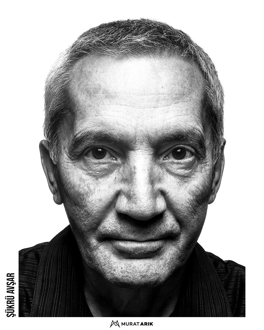 Black and white close-up portrait of an older man with short, graying hair, prominent facial wrinkles, and intense eyes, wearing a dark collared shirt.