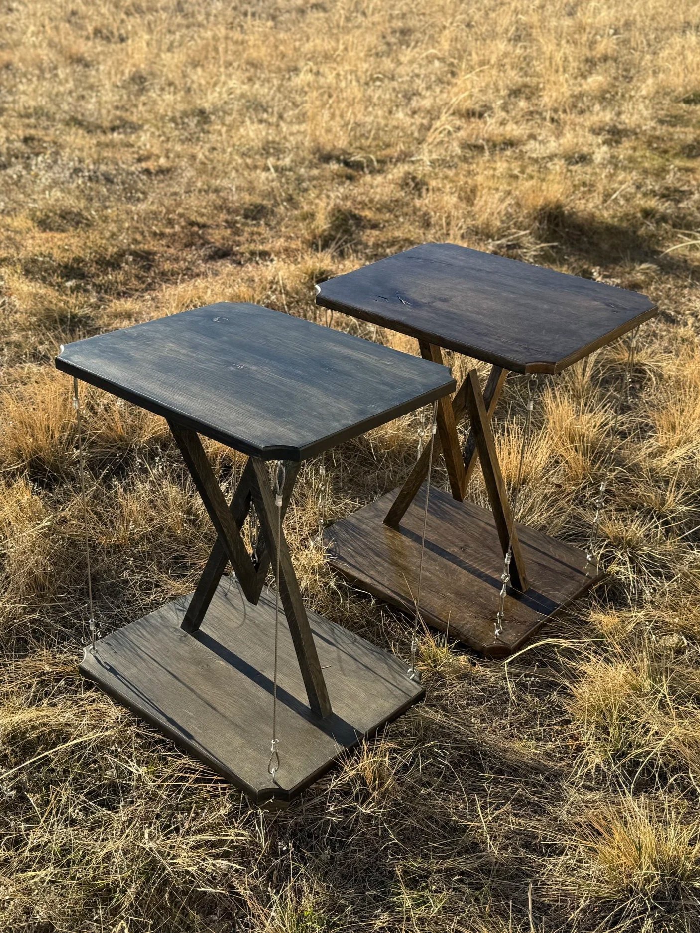 Two hanging wooden tables in a grassy field.