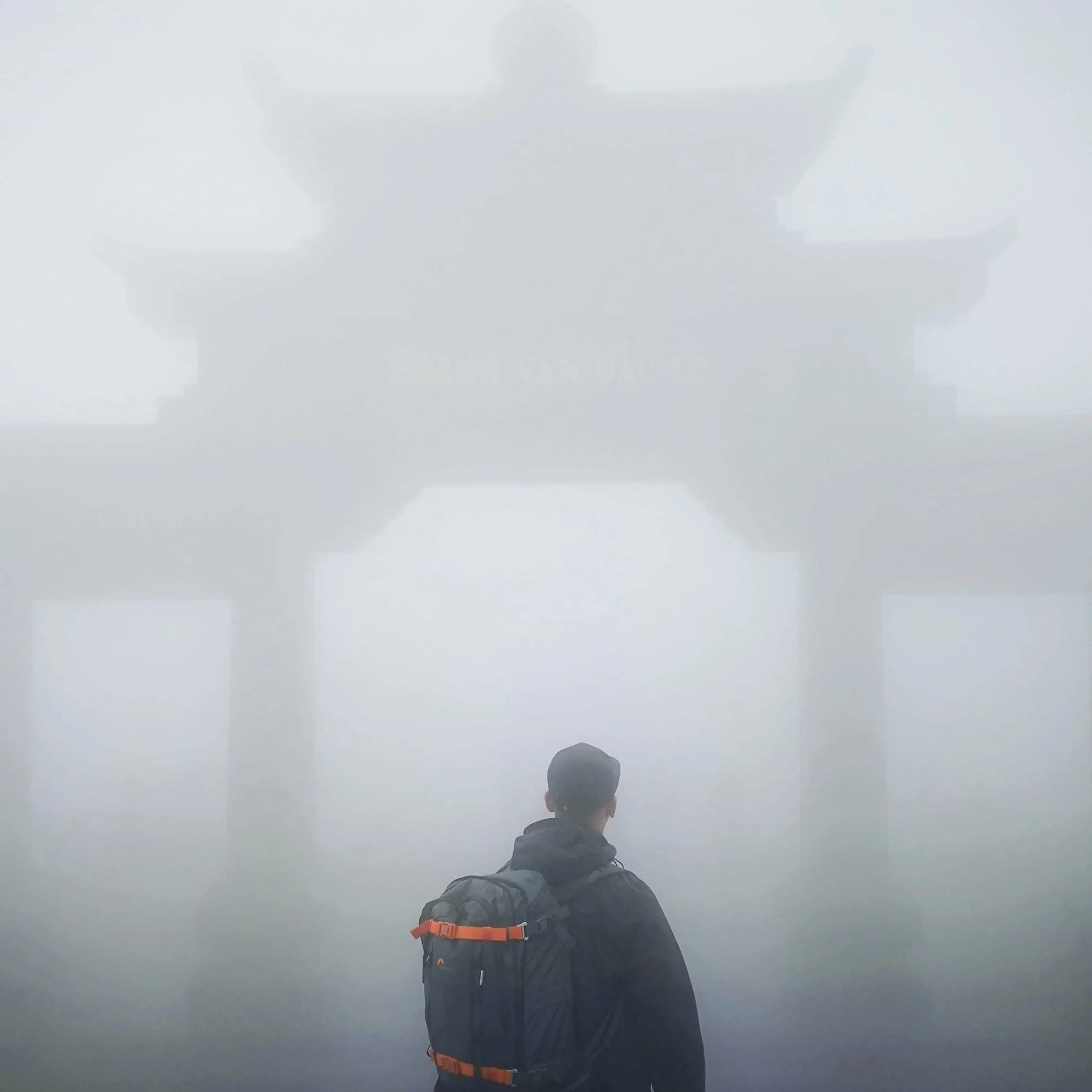 A person with a backpack standing in front of a foggy gateway with Chinese characters, surrounded by fog.