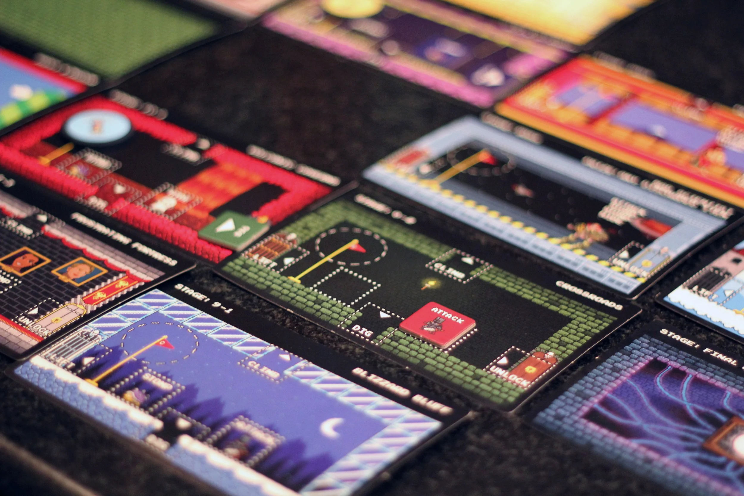 Collection of video game cards featuring pixel art designs of various video game scenes and characters, laid out on a black surface.