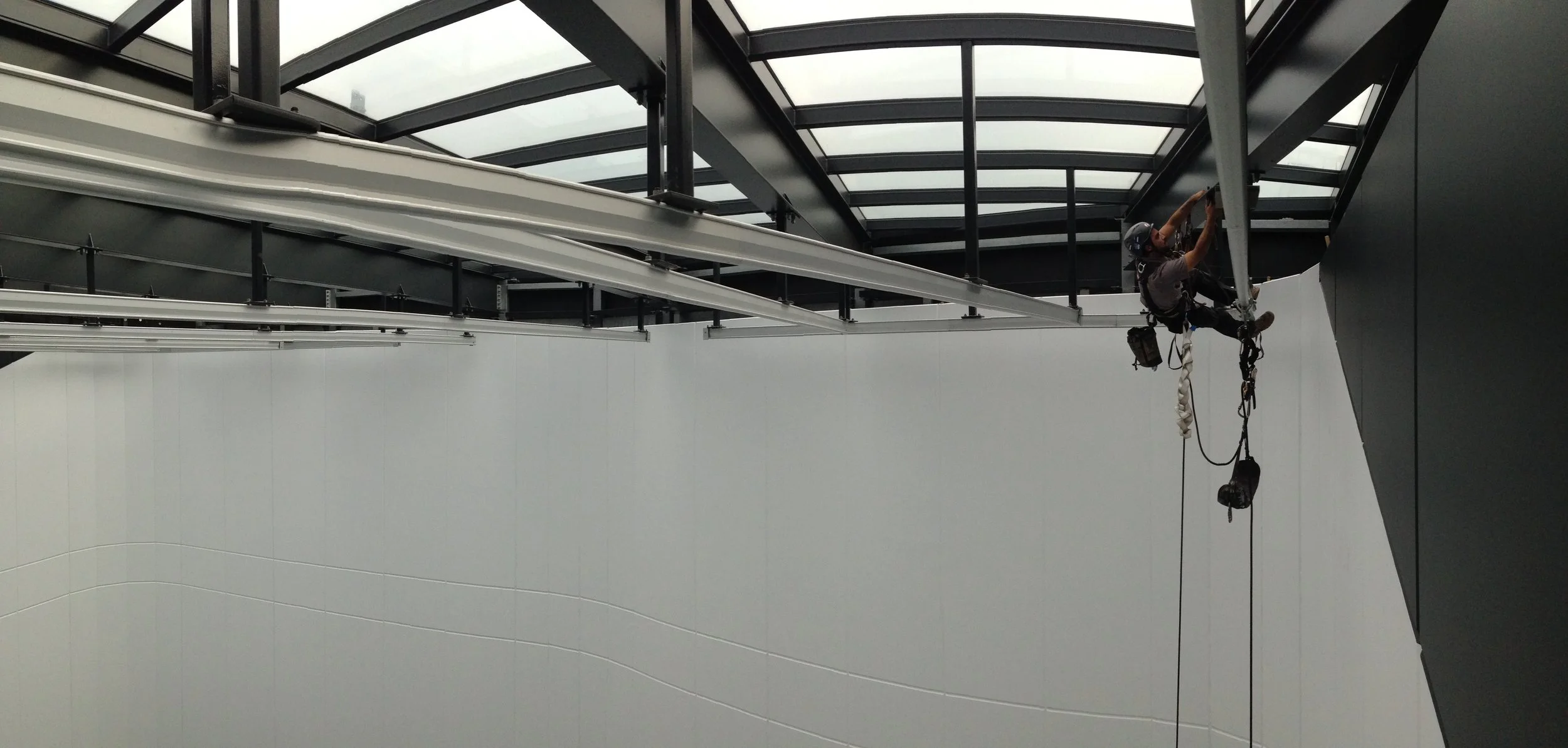 Rope access technician conducting maintenance on the ceiling framework inside a modern building.