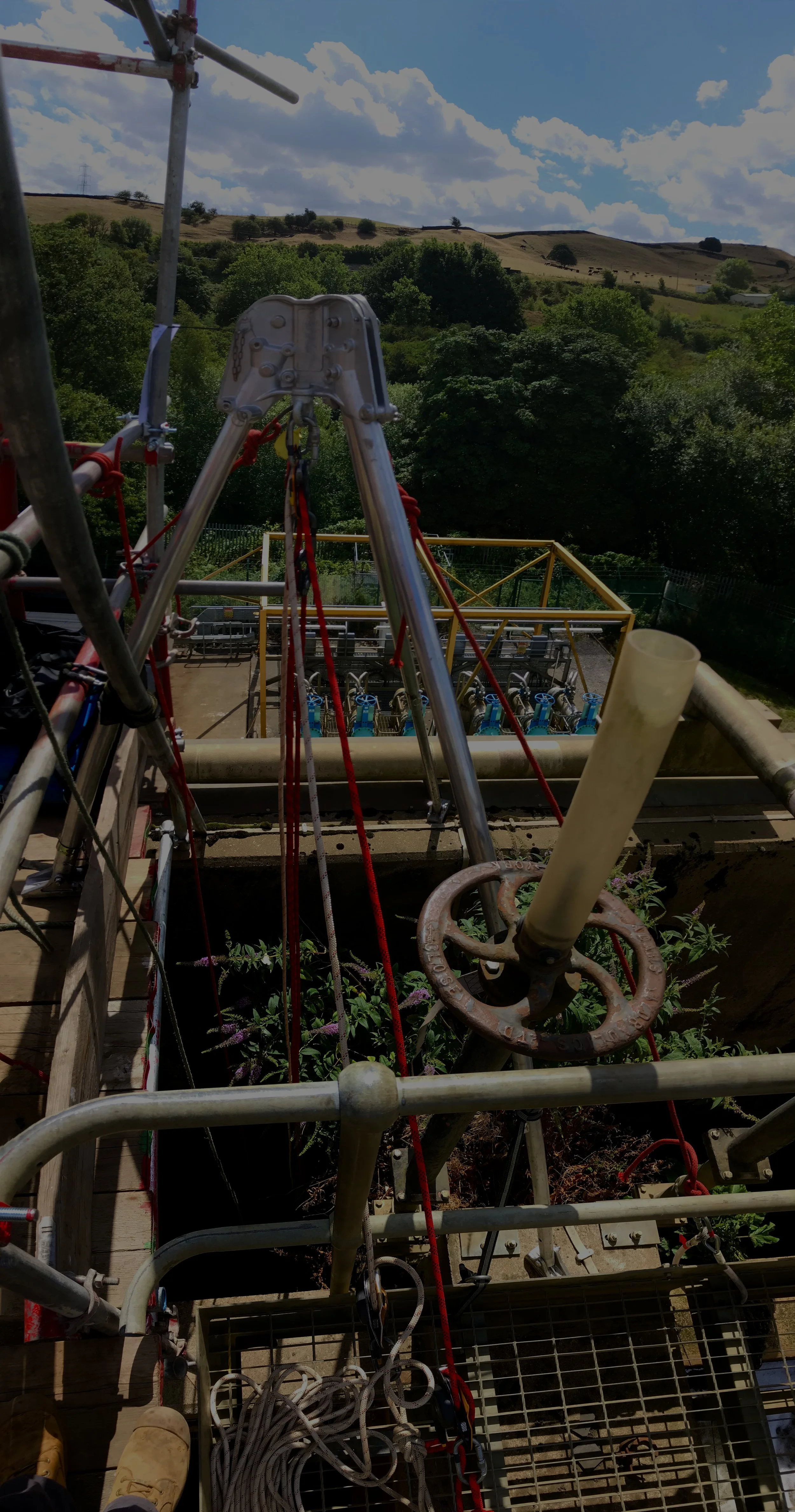View from a construction platform overlooking a landscape with green trees and rolling hills under a partly cloudy sky.