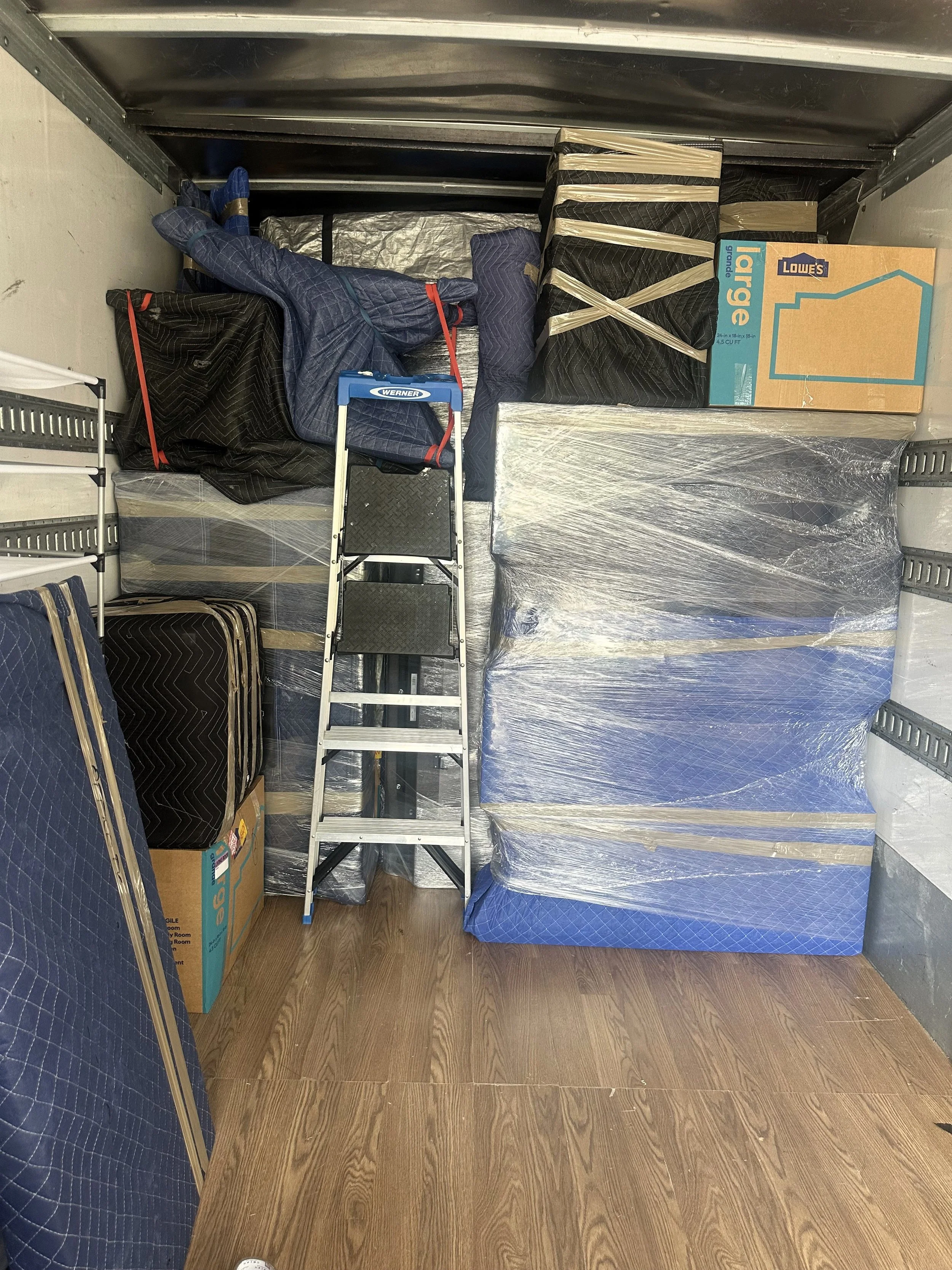 Moving truck loaded with furniture, boxes, and household items secured with protective blankets and wrapping materials.  Copy