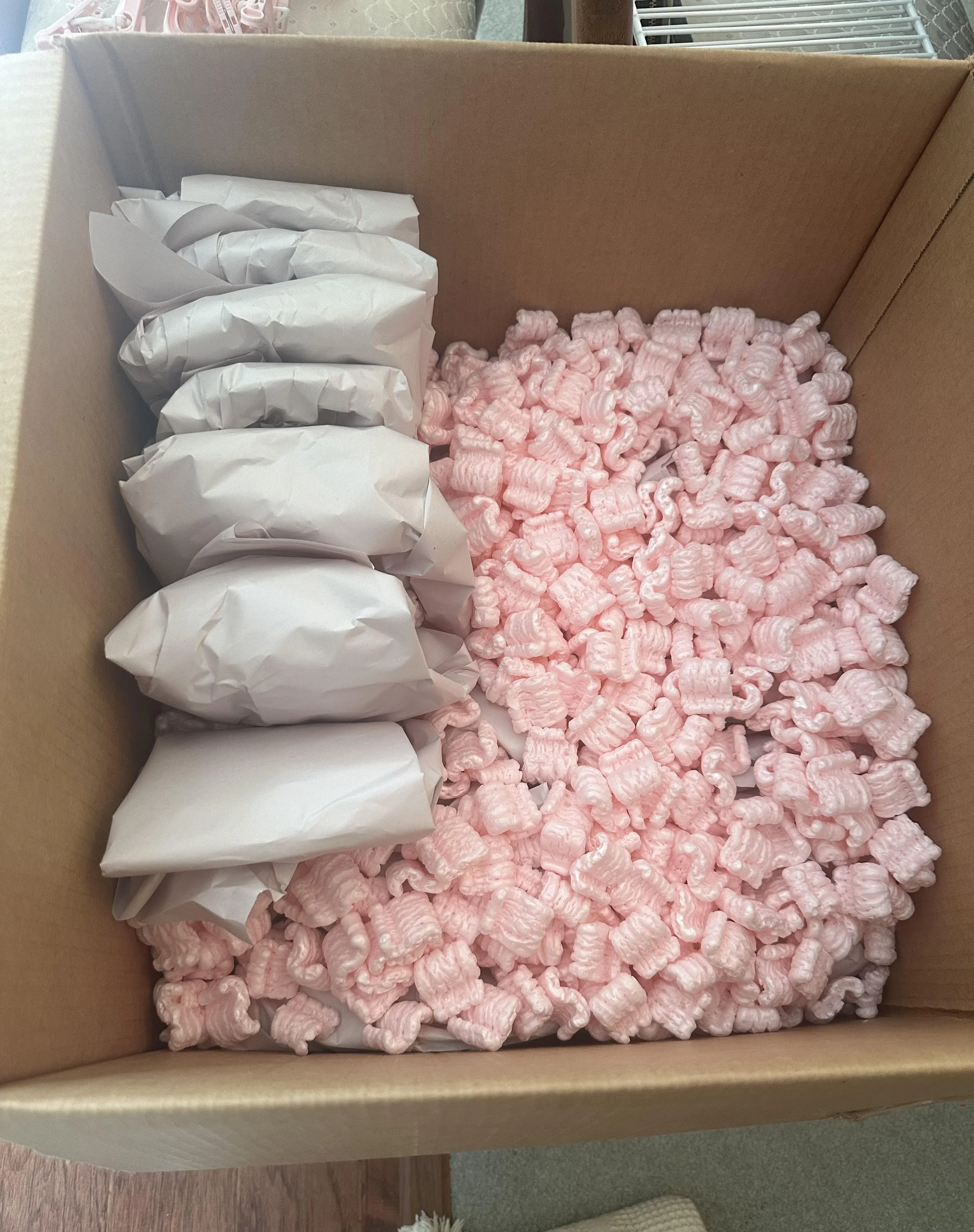 A large cardboard box filled with pink packing peanuts and several white wrapped items for a move by Easy Peasy Moving, LLC, in Central Florida.