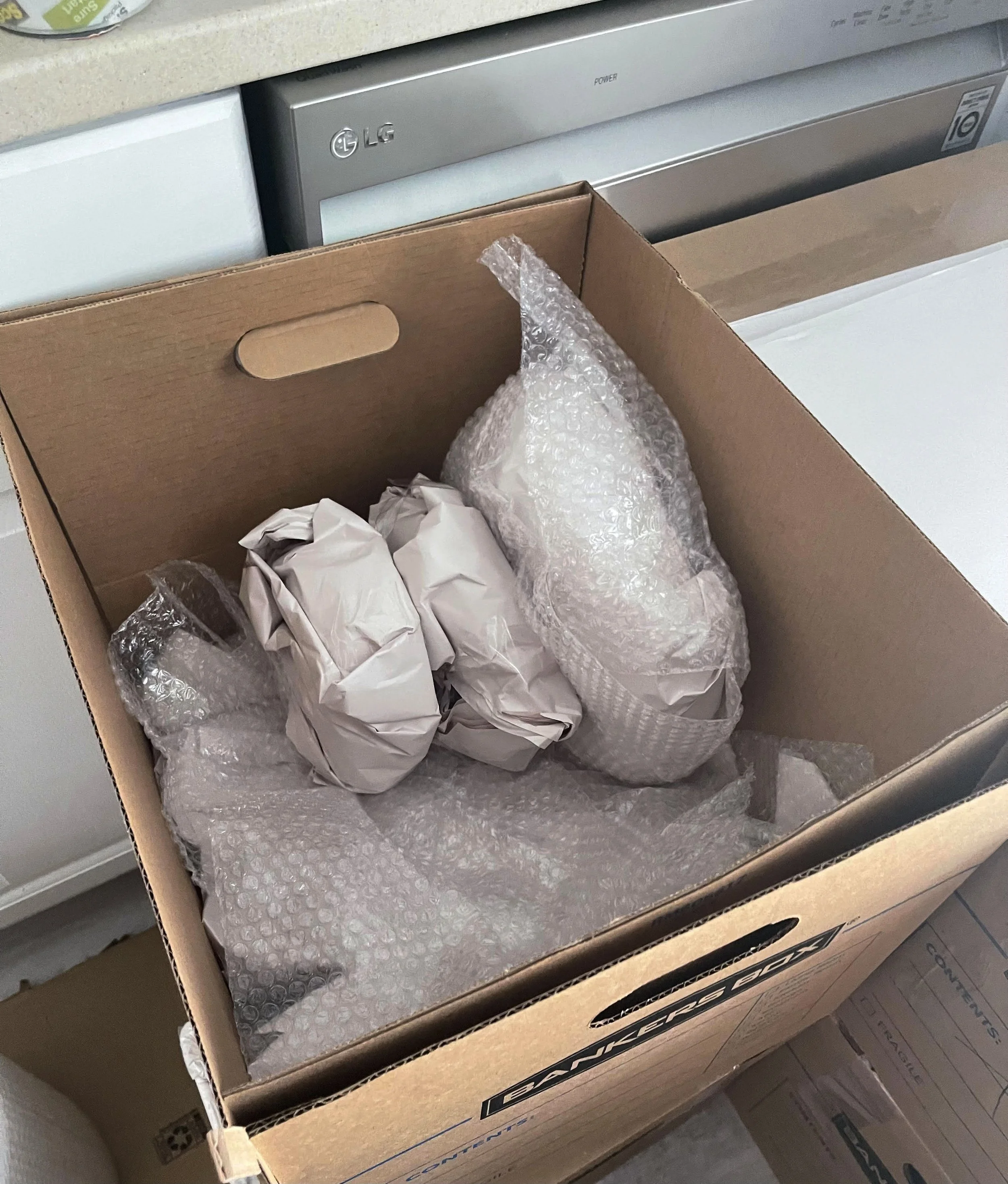 Open cardboard box containing wrapped white items and bubble wrap, prepared for a move by Easy Peasy Moving, LLC in Altamonte Springs, FL.
