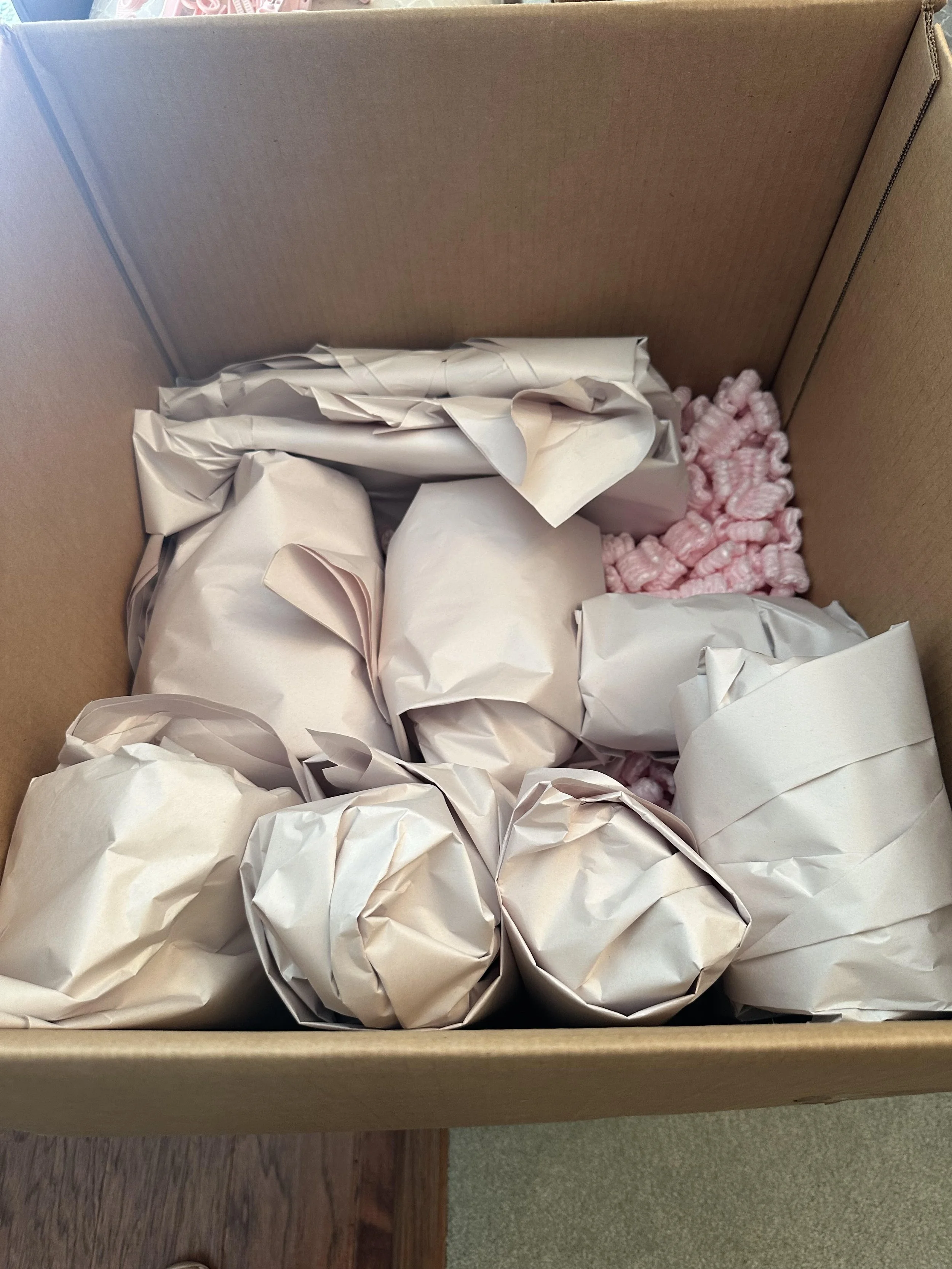 A cardboard box containing several wrapped items in white paper and pink packing peanuts by the moving company, Easy Peasy Moving, LLC, in Central Florida.