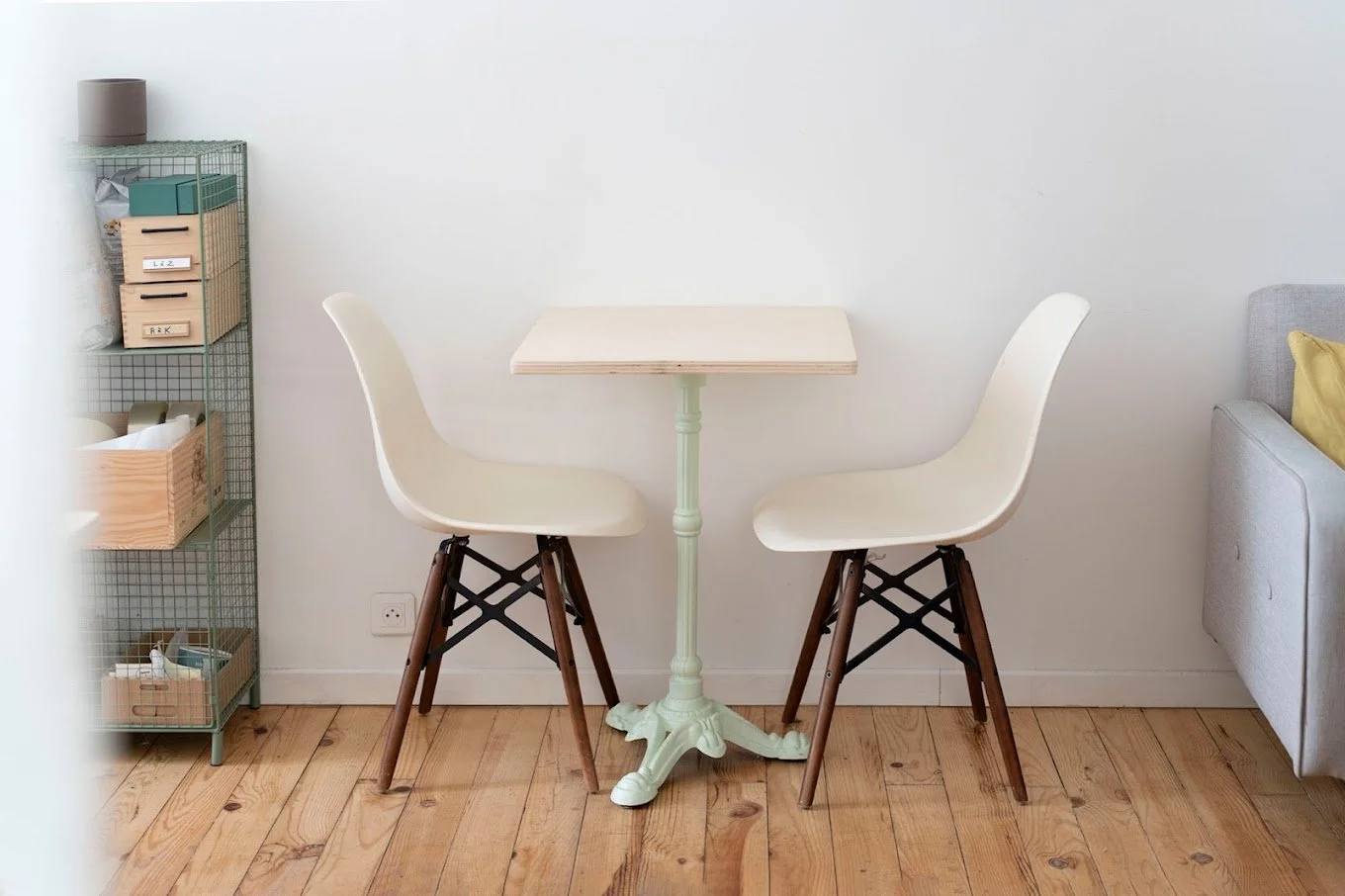 Une table à manger en bois blanc avec deux chaises modernes en plastique blanc, dans un intérieur minimaliste avec un sol en bois clair.