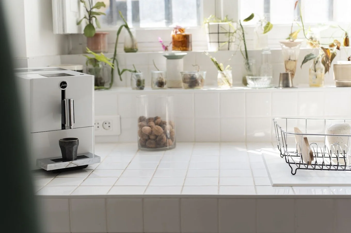 Une cuisine lumineuse avec un clavier à espresso blanc, un verre de biscuits, un évier, des plantes en pot sur le rebord de la fenêtre, et des accessoires de cuisine.