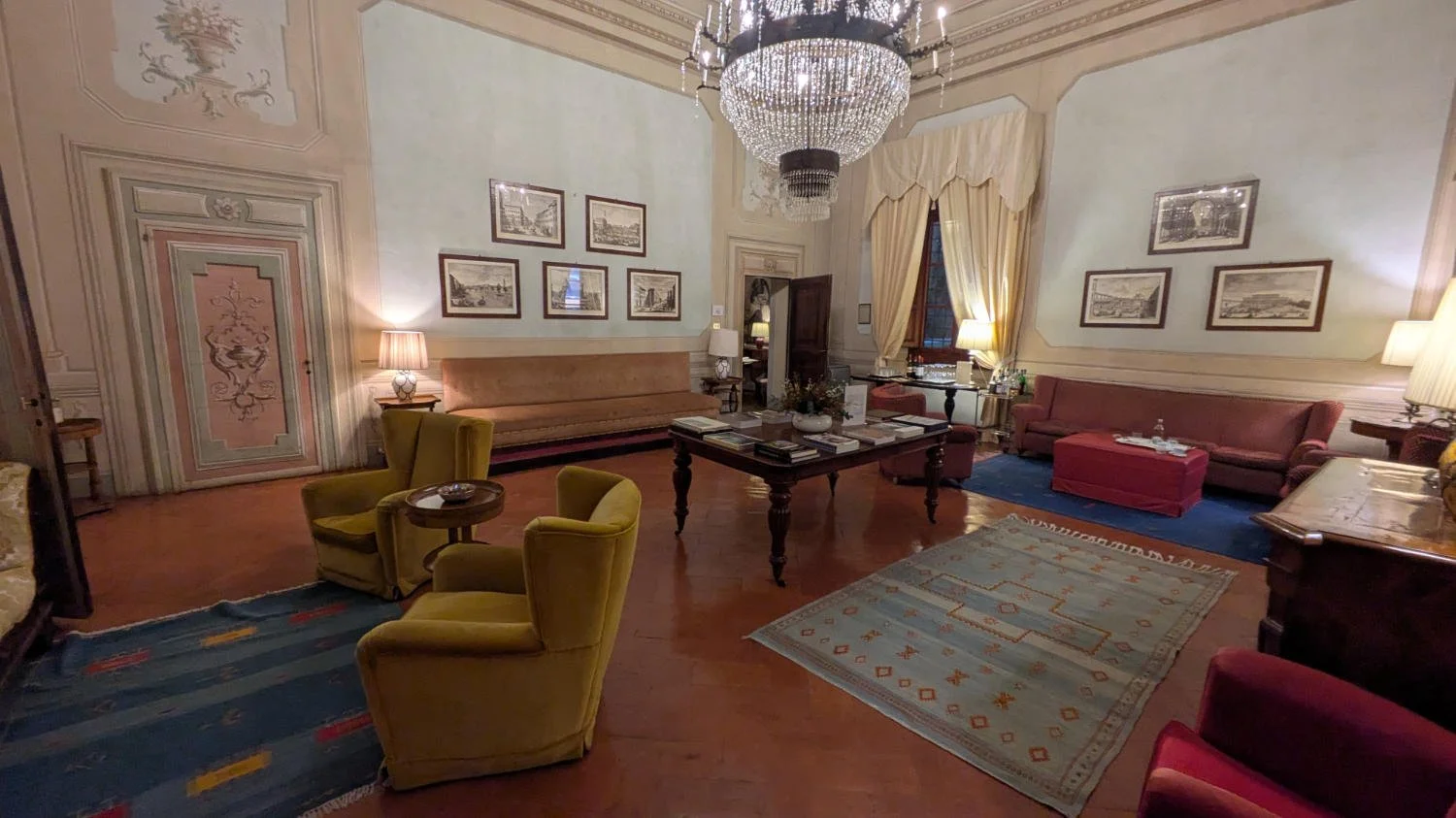 Elegant living room with antique furniture, chandeliers, framed artwork, and draped windows.
