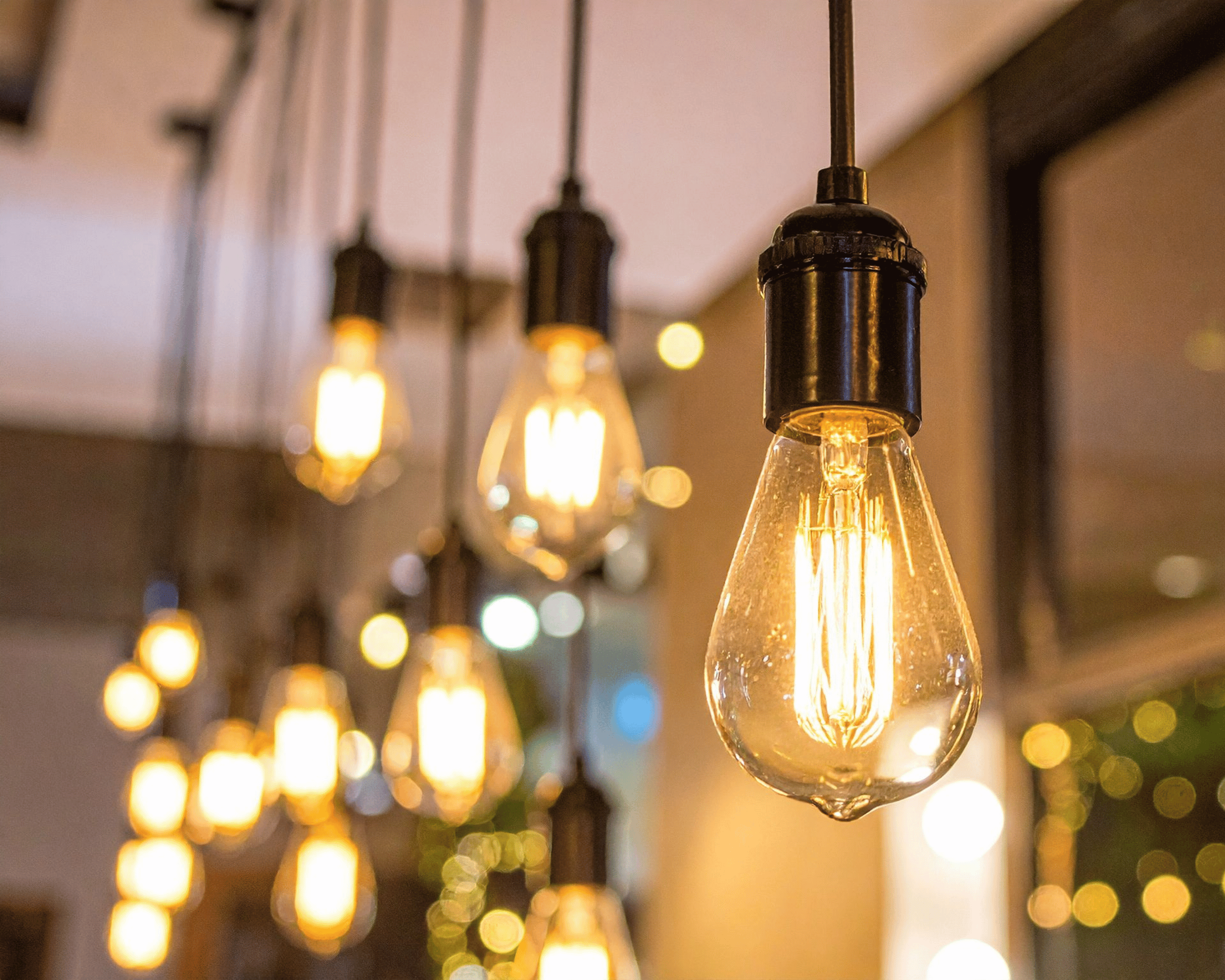Close-up of illuminated vintage Edison-style light bulbs hanging from the ceiling, with a warm glow and blurred background.