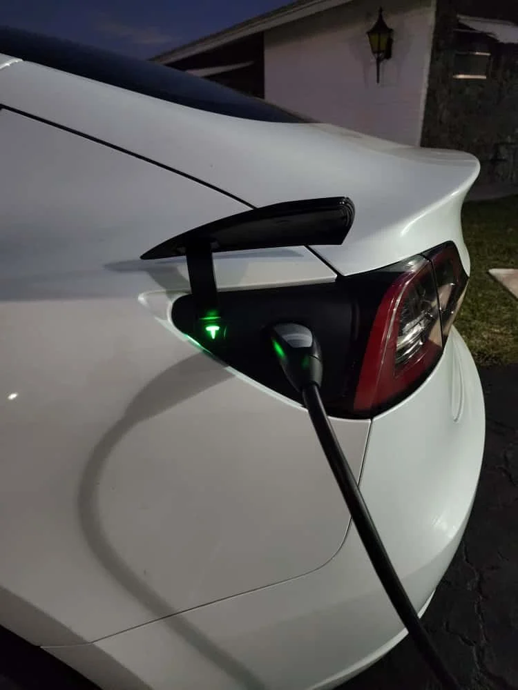 Close-up of a white EV charging at night, with a charging cable plugged into the car's charging port.