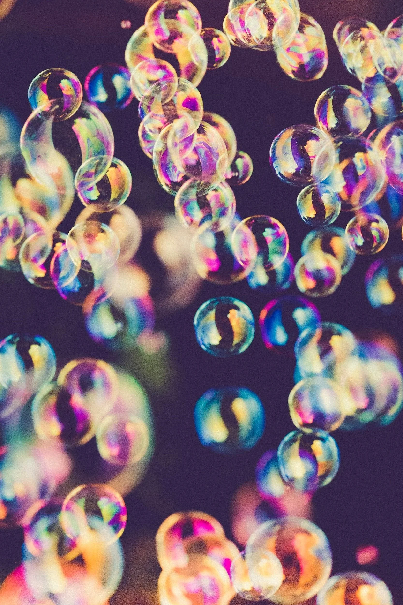 Bulles de savon colorées flottant dans l'air, en arrière-plan sombre.