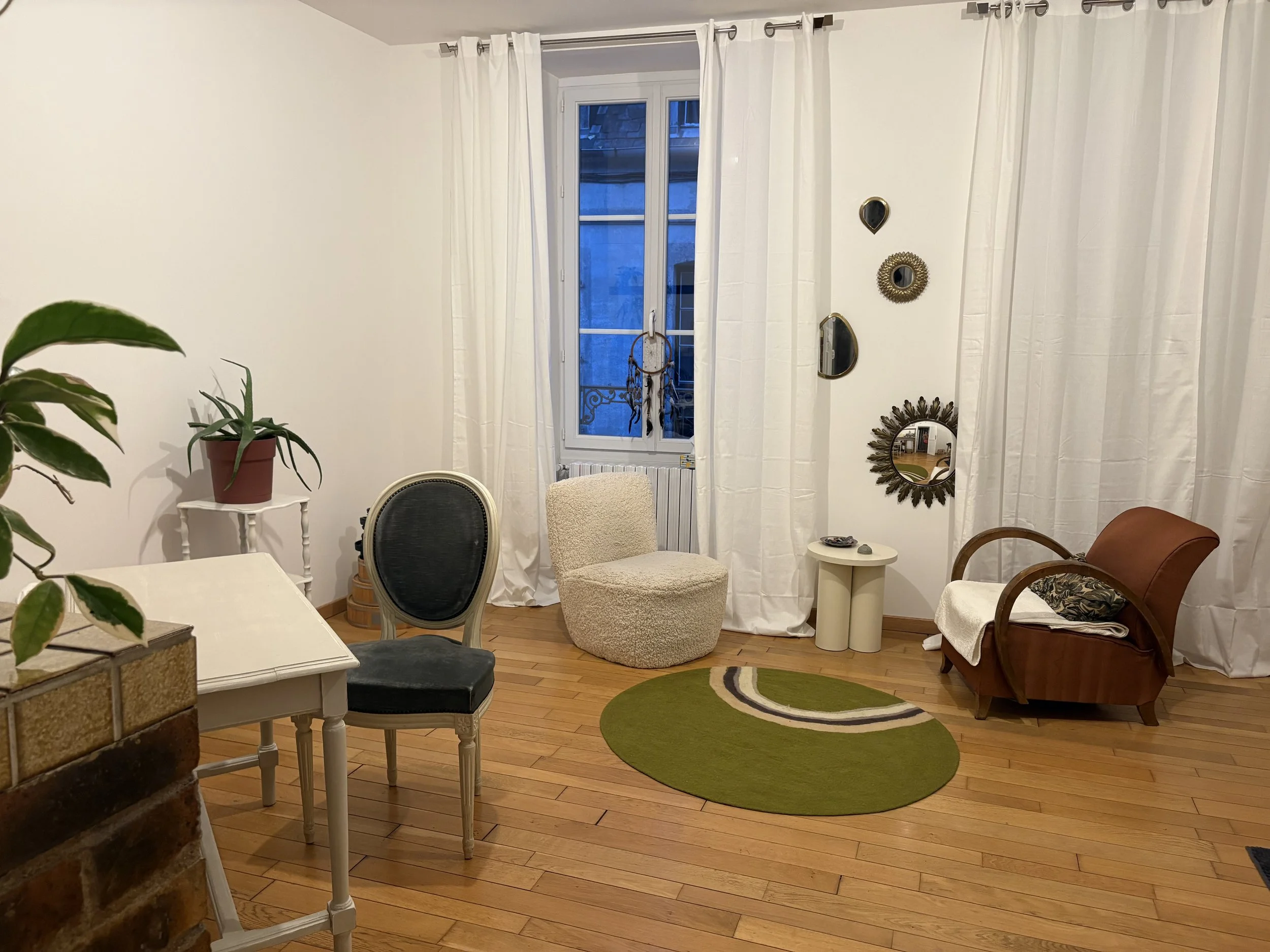 cabinet de consultation contenant un espace à part de conversations avec deux fauteuils individuels, à côté d'un mur décoré de différents miroirs, au sol un tapis vert en laine bouillie
