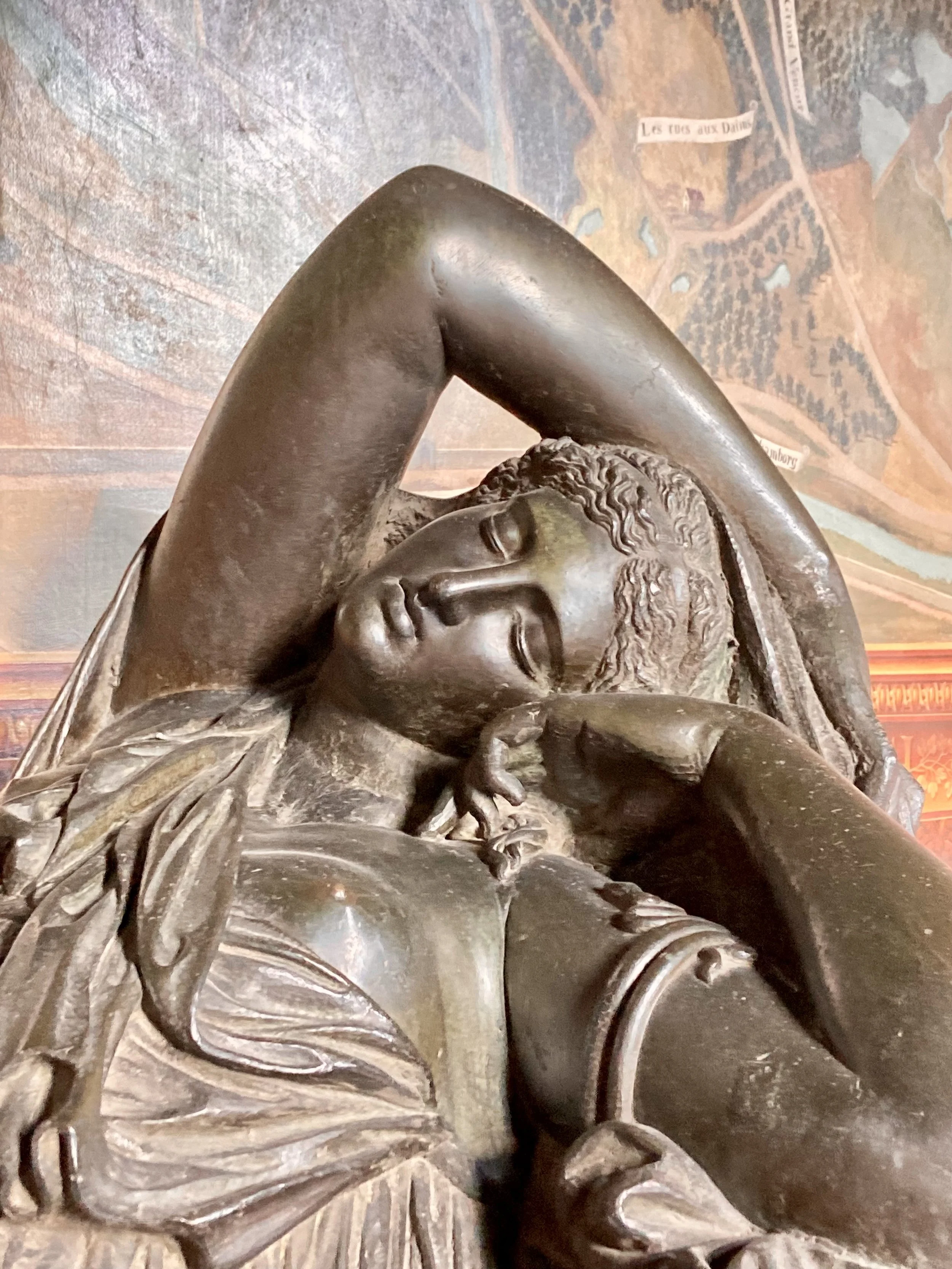 Sculpture en bronze représentant une femme avec ses bras levés, les yeux fermés, dans une pose expressive, avec une toile de fond représentant une carte ou un plan.