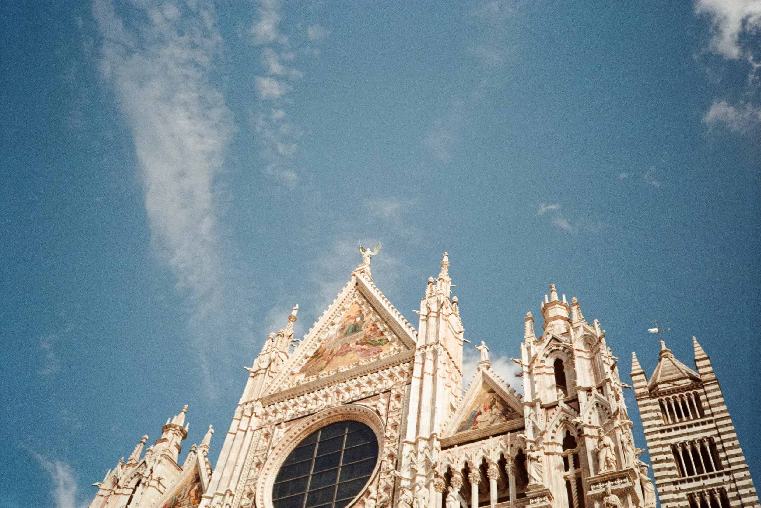 Close-up of the ornate facade of a Gothic cathedral with pointed arches, statues, and detailed stonework, against a blue sky with a few clouds.