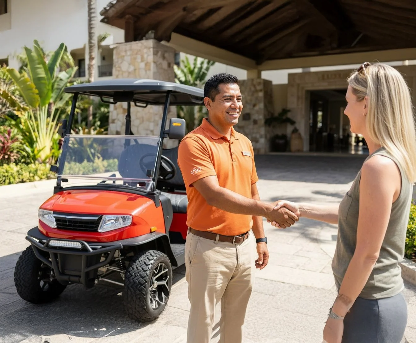 A man in an orange polo shirt and beige pants shaking hands with a woman in a sleeveless top, standing outdoors near a red golf cart in front of a building with tropical plants.