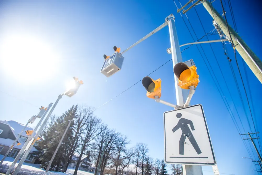 Traffic lights and pedestrian crossing sign under a bright blue sky with sunlight.