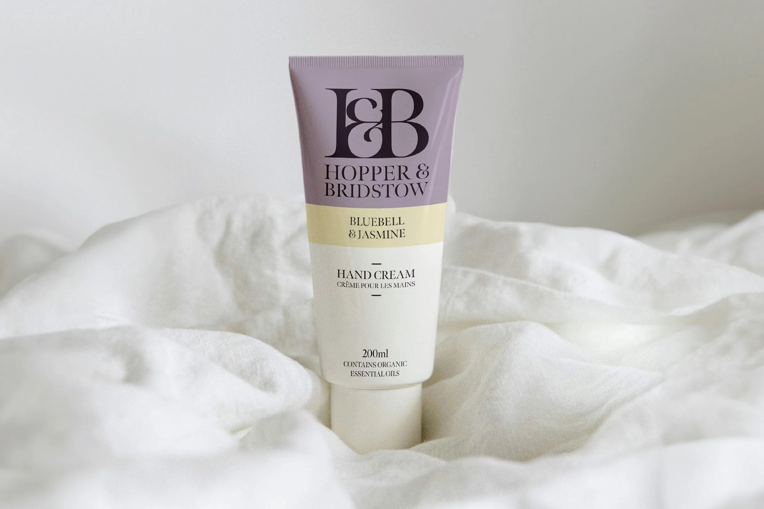 A tube of Hopper & Bridstow Bluebell & Jasmine hand cream standing on soft white fabric.