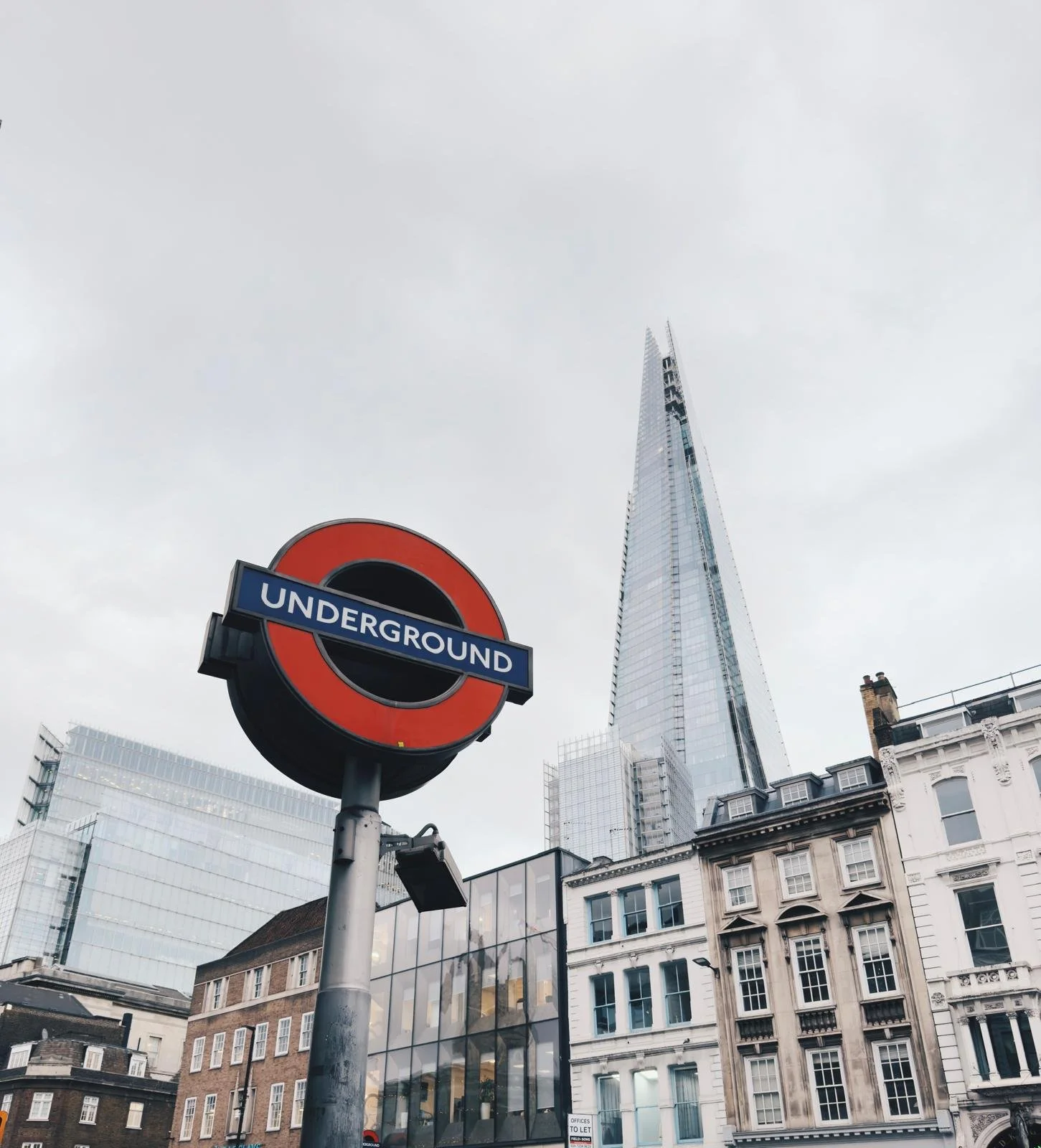 London Underground sign with a modern skyscraper in the background on a cloudy day.