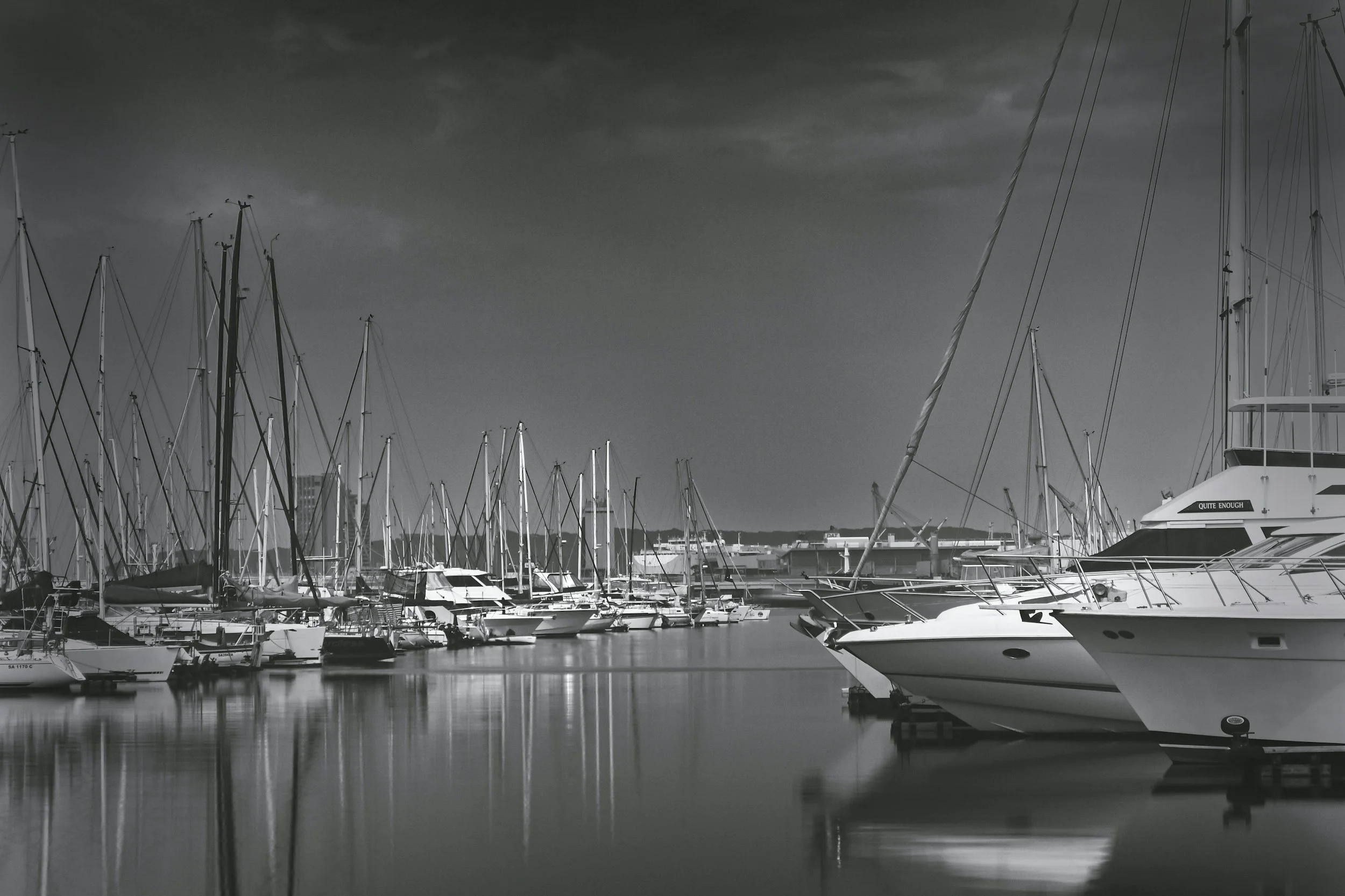 Motor yachts and sailboats docked at a marina under a dark, cloudy sky with reflections on the water.