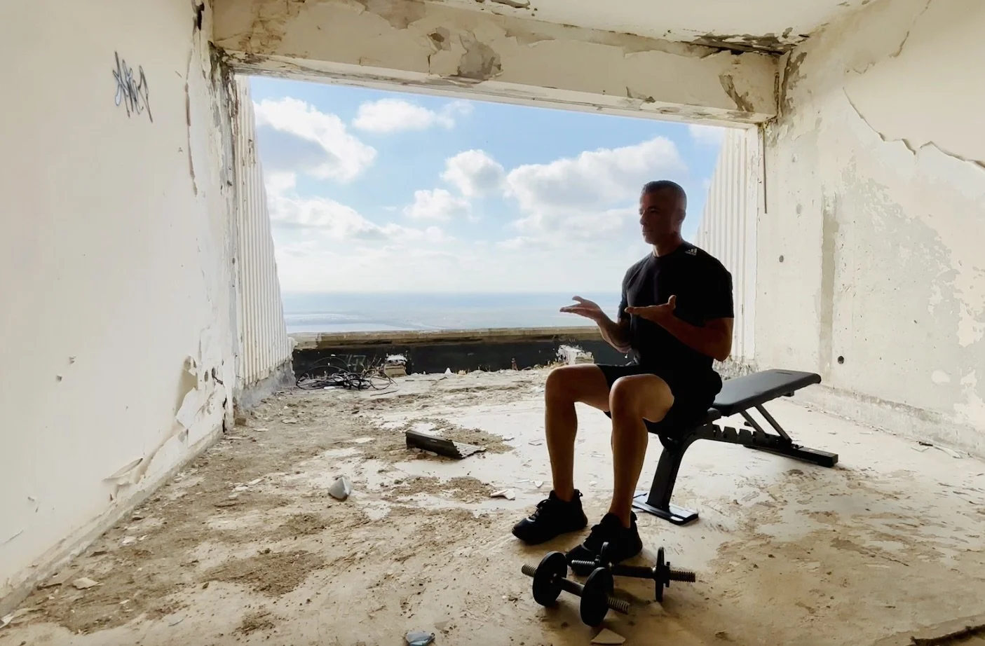 Photo of a man seated on a workout bench with his hands out in front of him during a breathing exercise