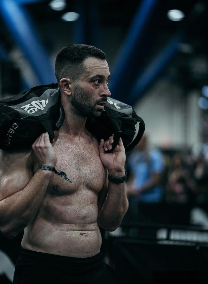 Shirtless man carrying a heavy sandbag over his shoulders
