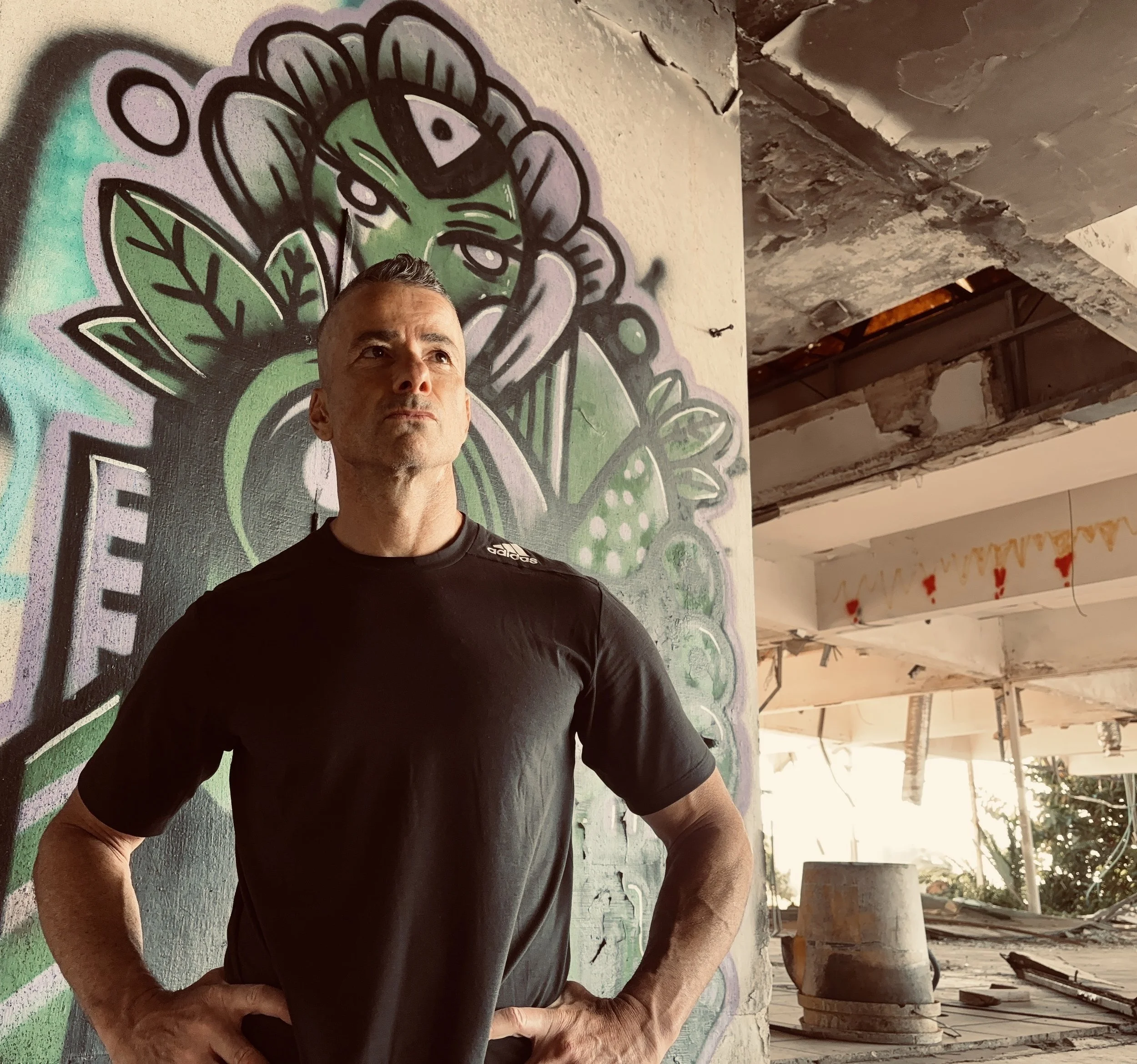 Photo of a man with his hands on his hips in front of wall with graffiti art