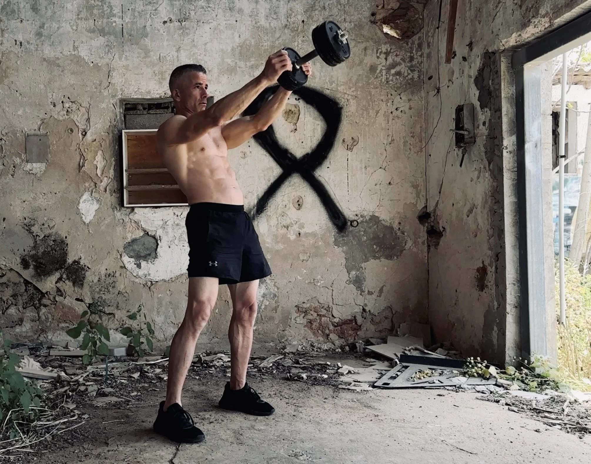 Man in black shorts swinging a dumbbell at eye level