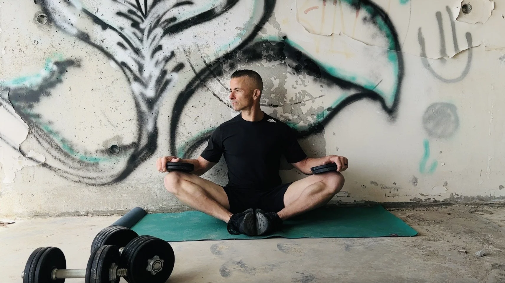 Photo of a man seated in a weighted butterfly stretch on a green yoga mat