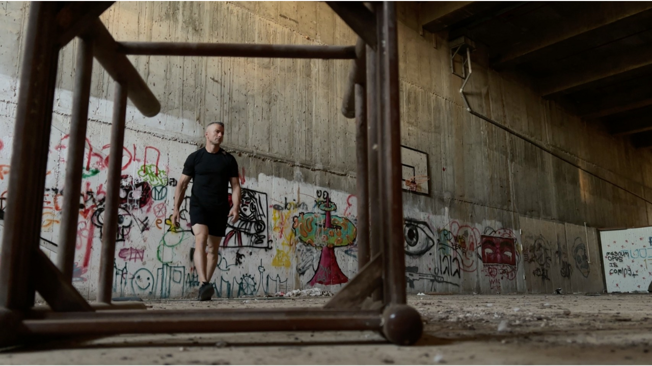 Man in black t-shirt and shorts walking through an abandoned building.