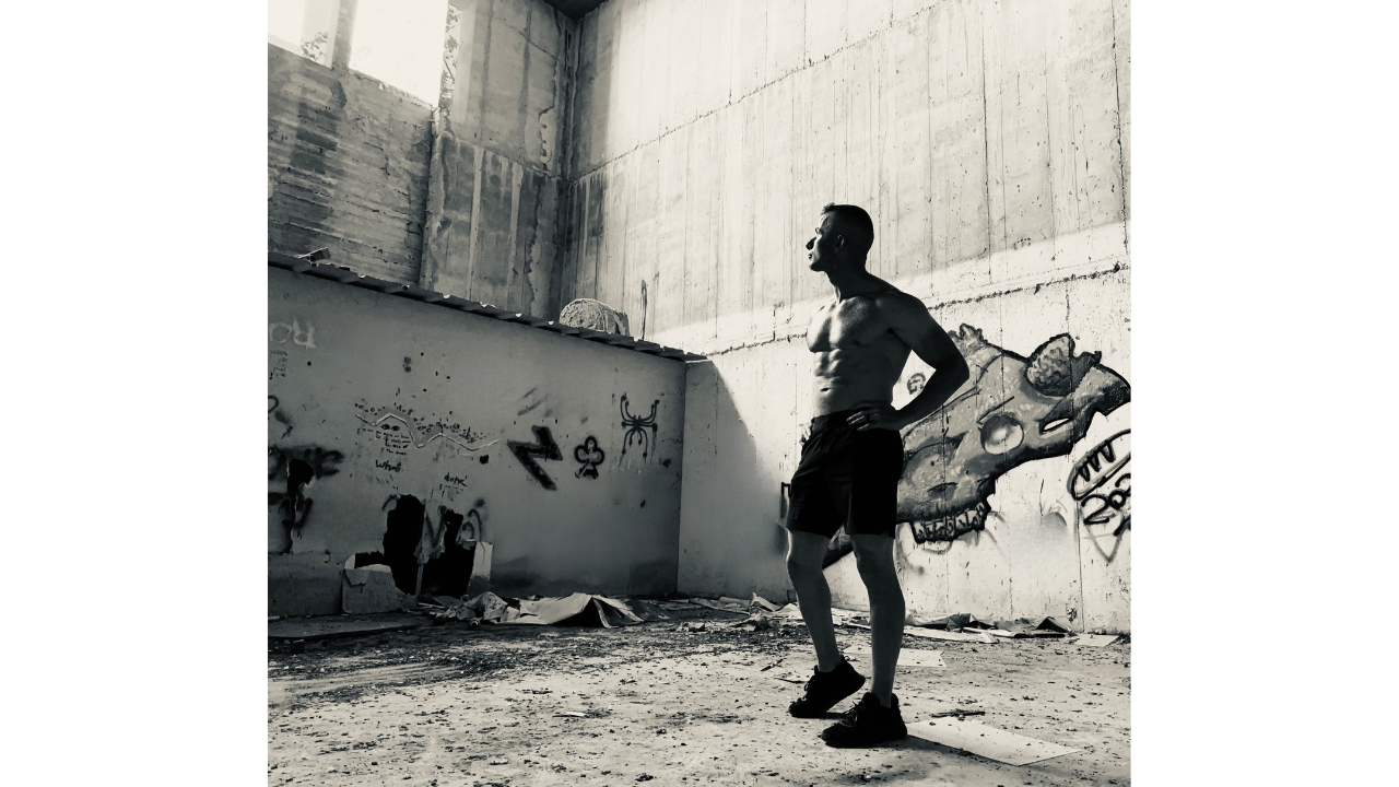 Shirtless man looking up at a light source in an abandoned building