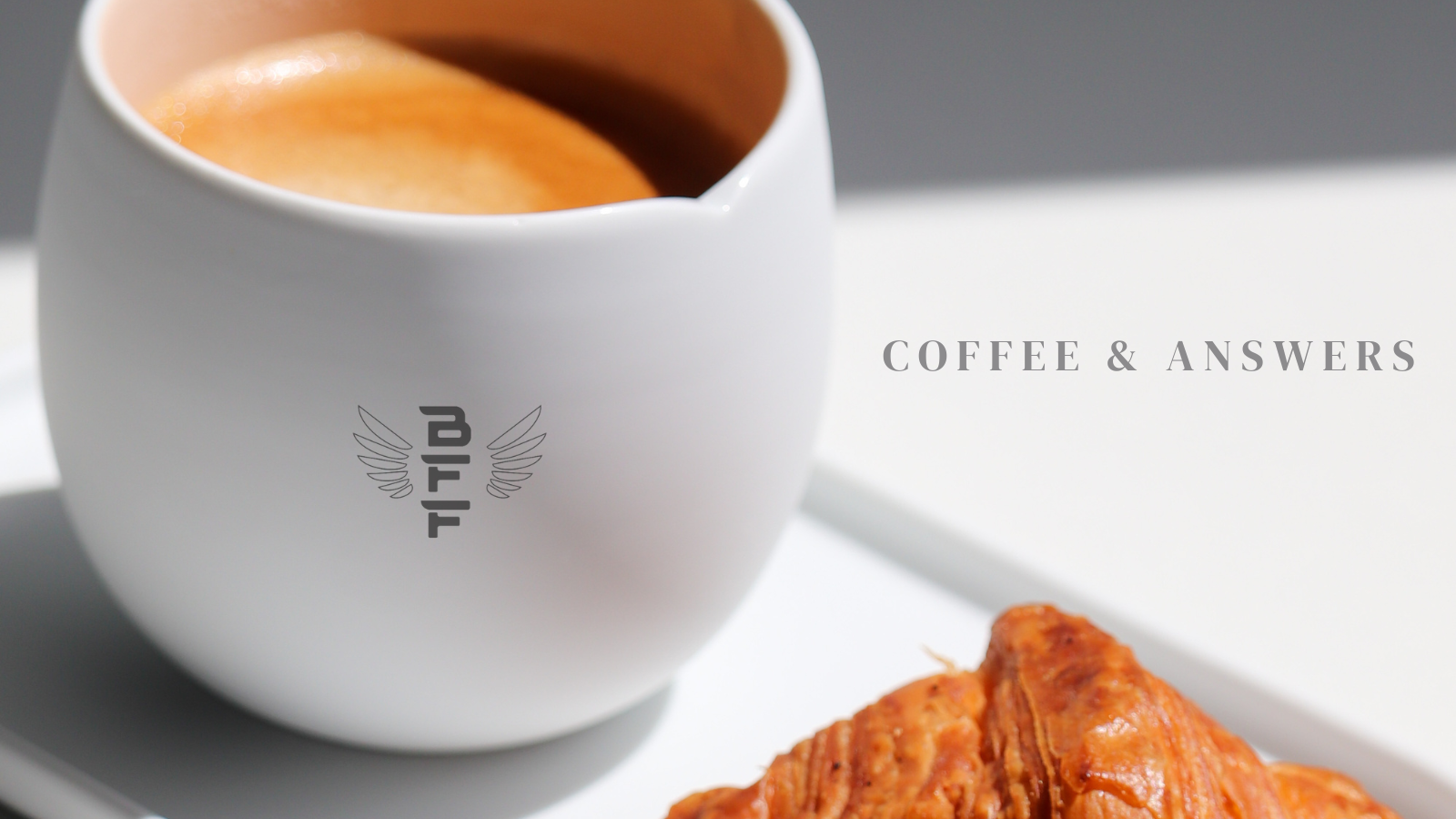 Close-up of a white coffee cup filled with coffee and a croissant on a white plate, with text "Coffee & Answers" on the image.