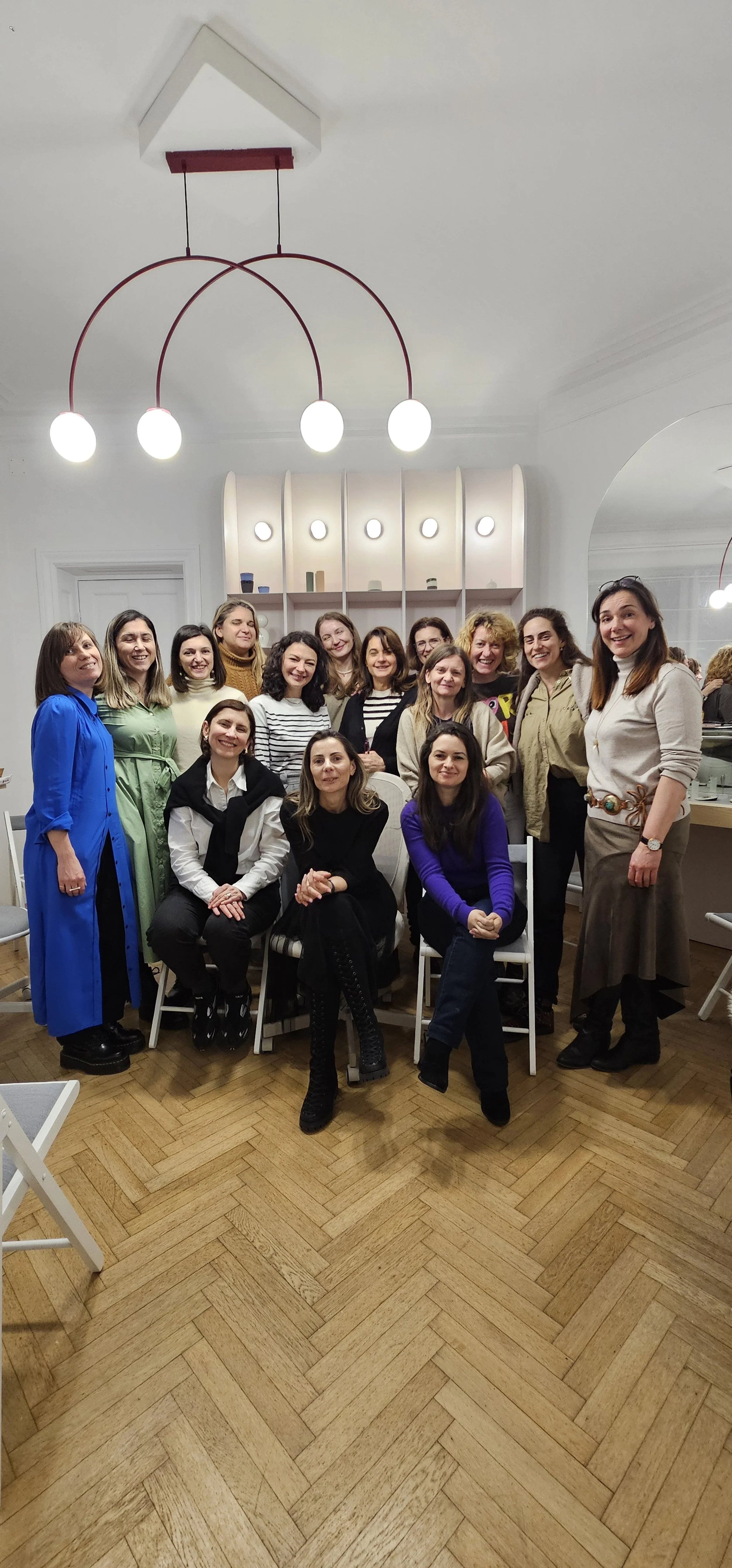 Group of women gathered indoors, posing for a photo, some seated and some standing, in a well-lit room with modern decor.