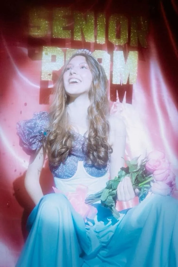 Catwoman wearing a sparkly outfit with puffy sleeves, holding a bouquet of pink roses, and smiling against a backdrop with the text 'Benson Program' in gold letters.