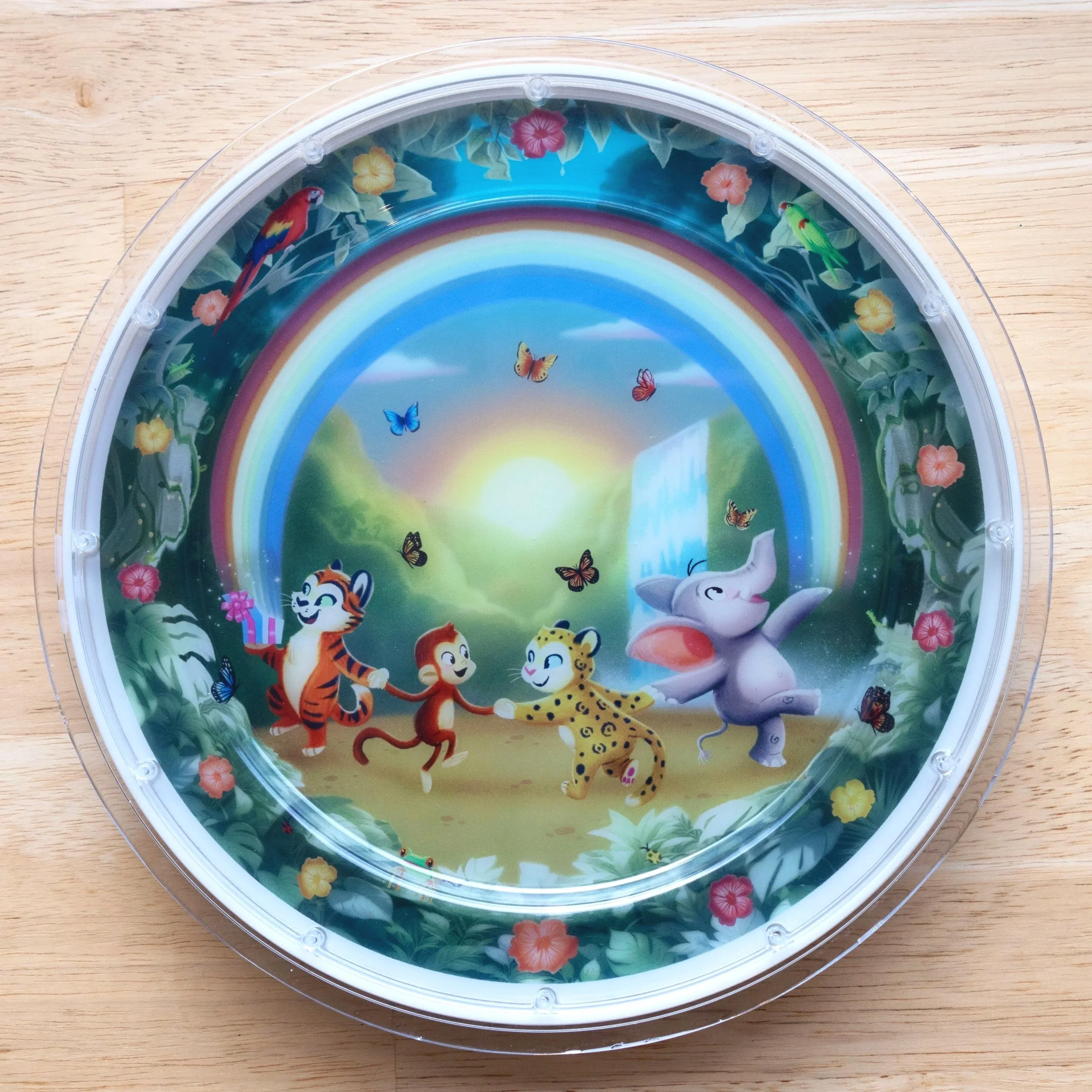 Colorful children's plate with a jungle scene featuring animated animals dancing, butterflies, a rainbow, and a waterfall.