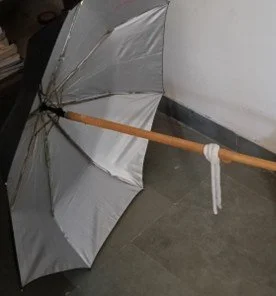 A silver umbrella with a wooden handle lying on the floor against a wall.